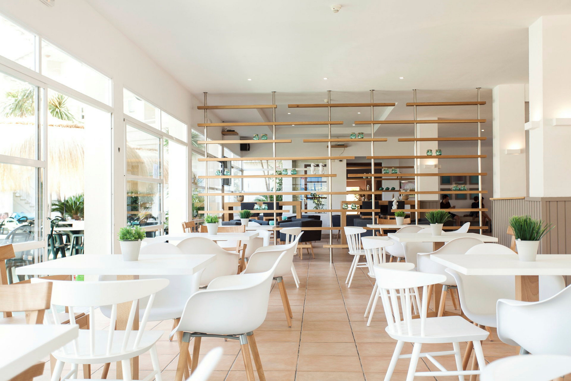 Valoisa ja moderni ravintola, jossa valkoiset huonekalut ja vihreitä kasveja. (Tekoälyn luoma teksti)