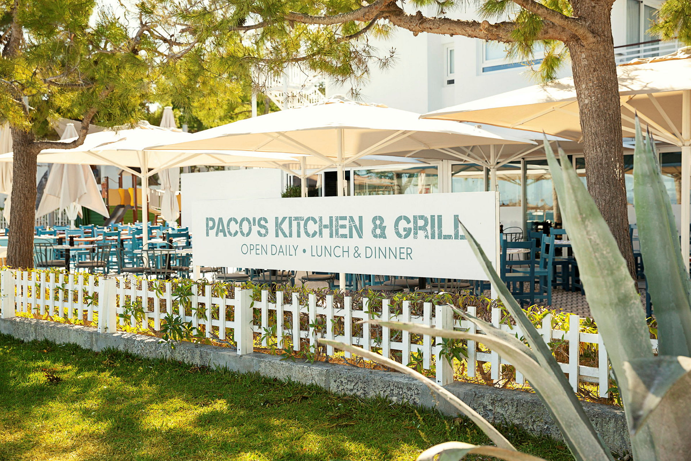 Kyltti, jossa lukee 'Paco's Kitchen & Grill' ravintolan ulkoterassin edessä. (Tekoälyn luoma teksti)