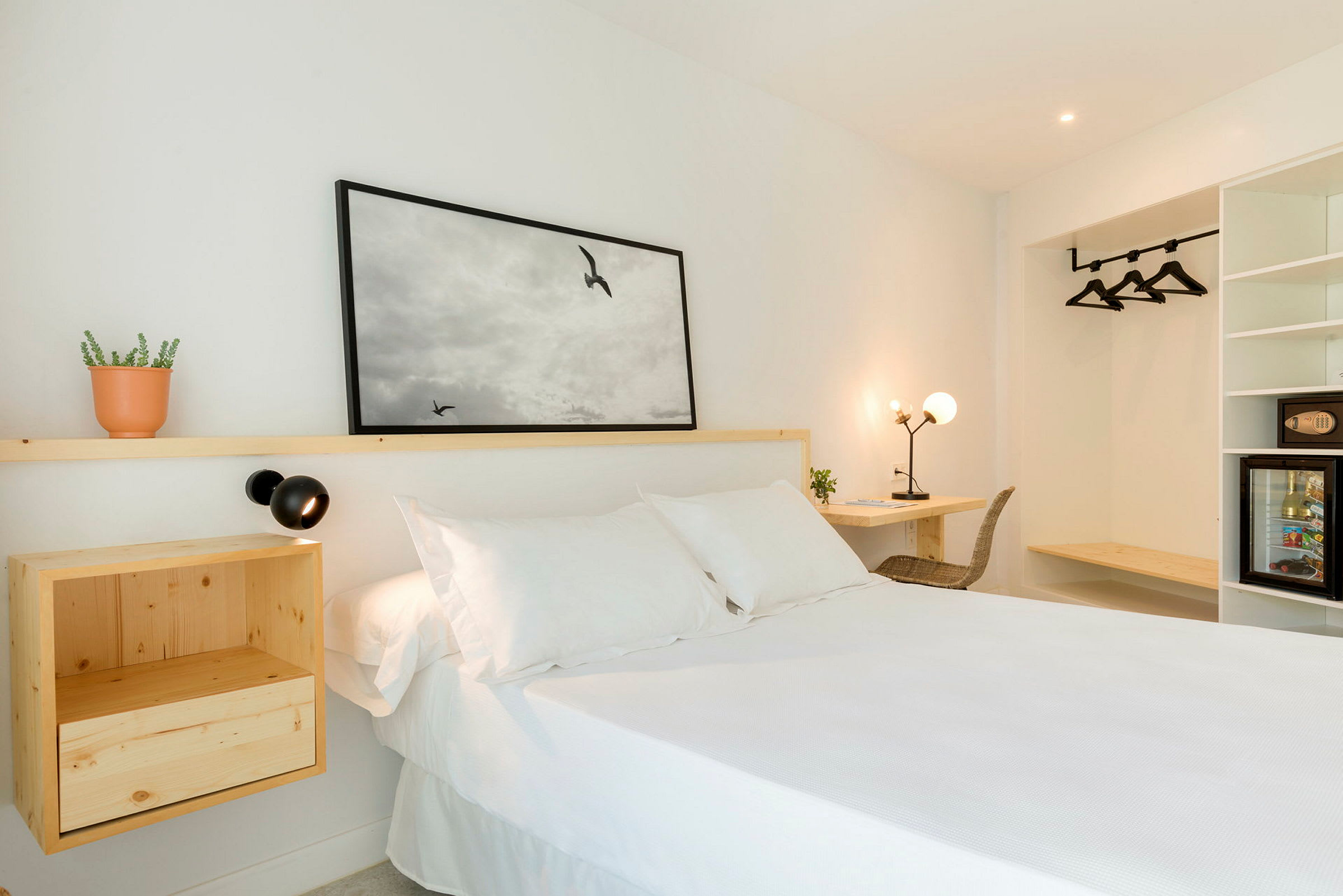 Vaalea hotellihuone, jossa on valkoinen sänky, puiset huonekalut ja seinäkoriste. (Tekoälyn luoma teksti)