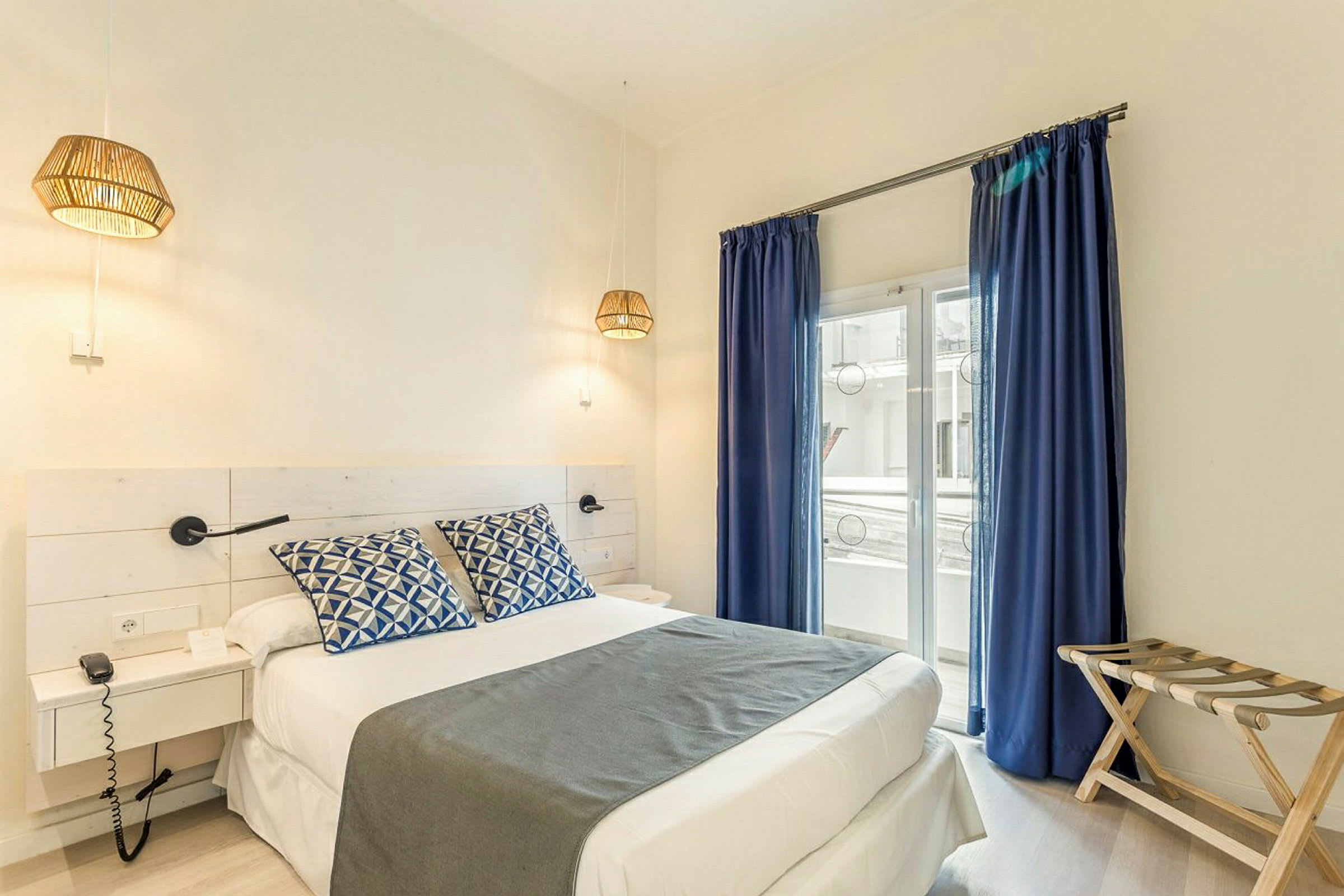Hotellihuone, jossa on parivuode, siniset verhot ja ikkuna parvekkeelle. (Tekoälyn luoma teksti)