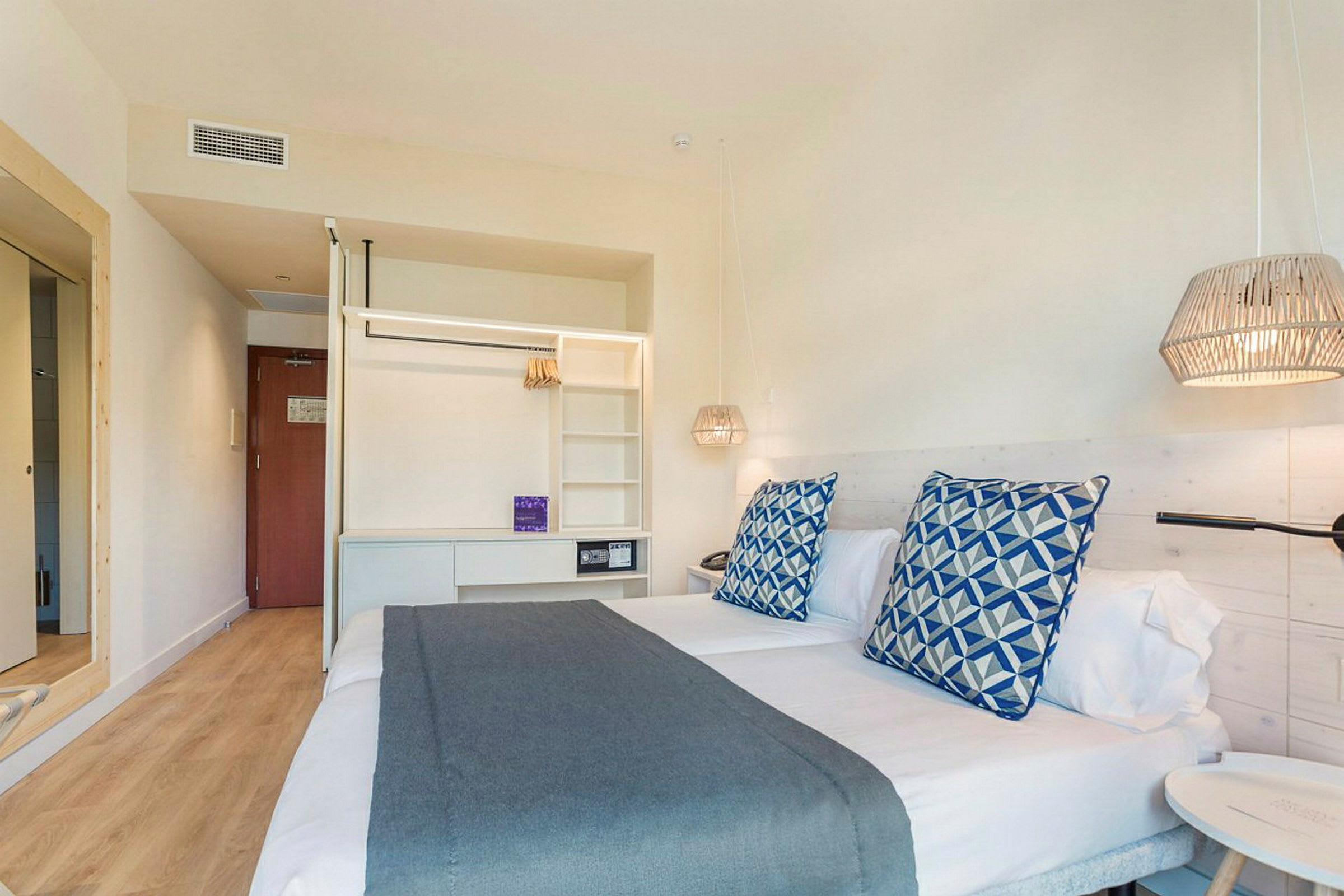 Hotellihuoneen sisätila, jossa kaksi yhden hengen sänkyä, koristeelliset tyynyt ja sängyn valaisimet. (Tekoälyn luoma teksti)