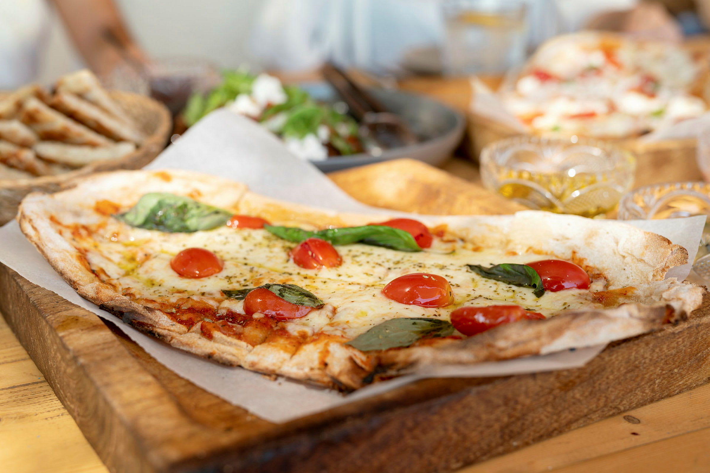 Neliskulmainen pizza, jossa on tomaattia ja basilikaa puulautasella. (Tekoälyn luoma teksti)