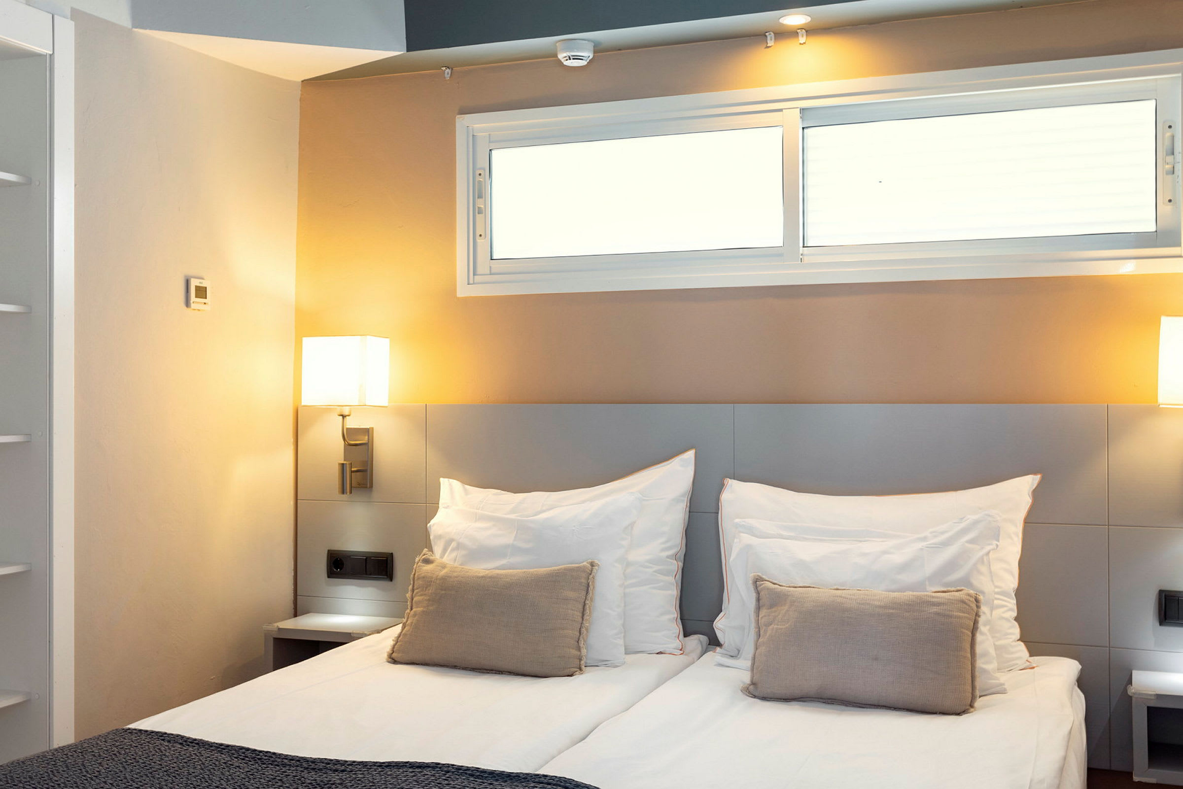 Hotellihuone, jossa on parivuode, koristeellinen tyyny ja sängyn vieressä olevat lamput. (Tekoälyn luoma teksti)