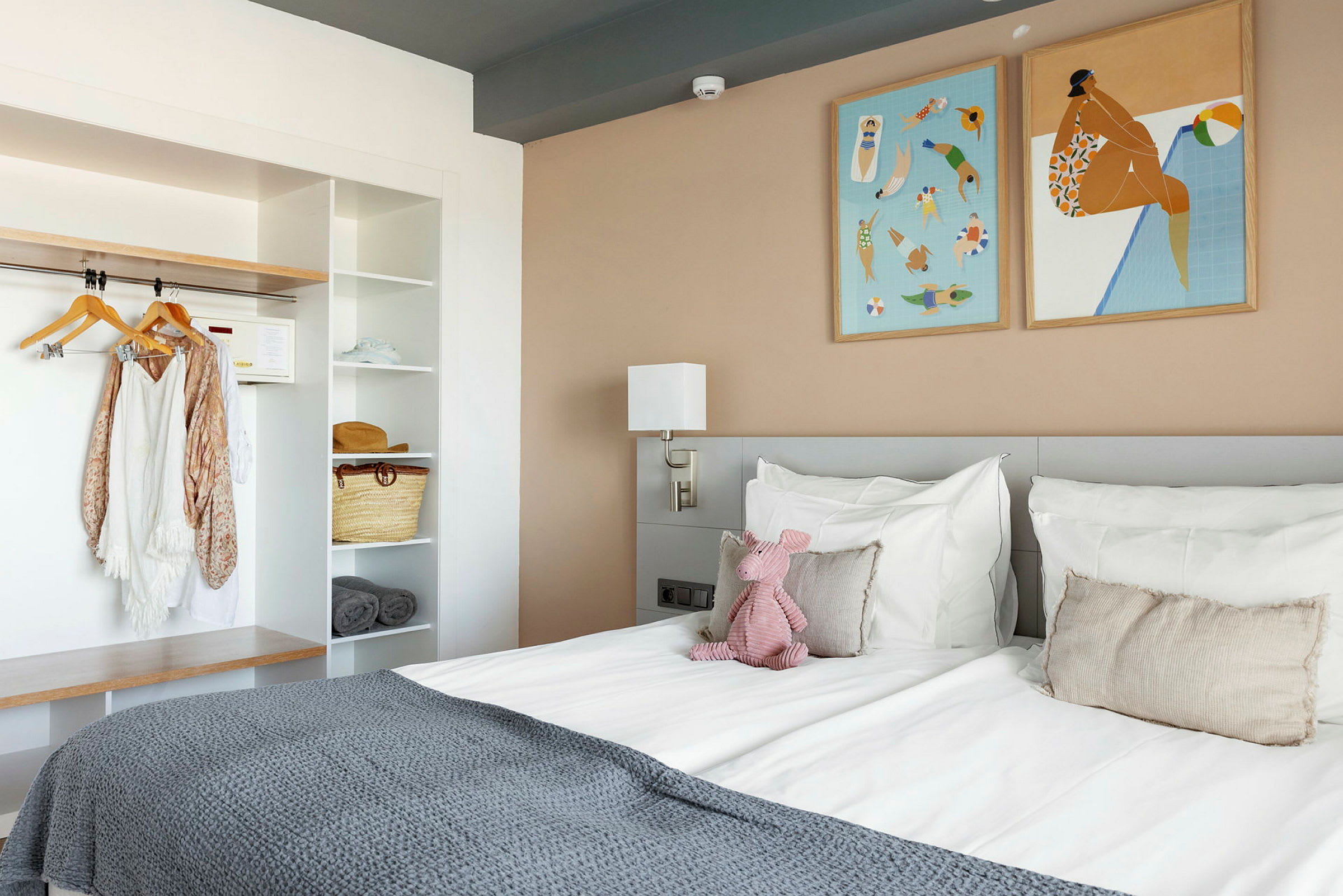 Hotellihuone, jossa on sänky, seinätaidetta ja hylly. (Tekoälyn luoma teksti)