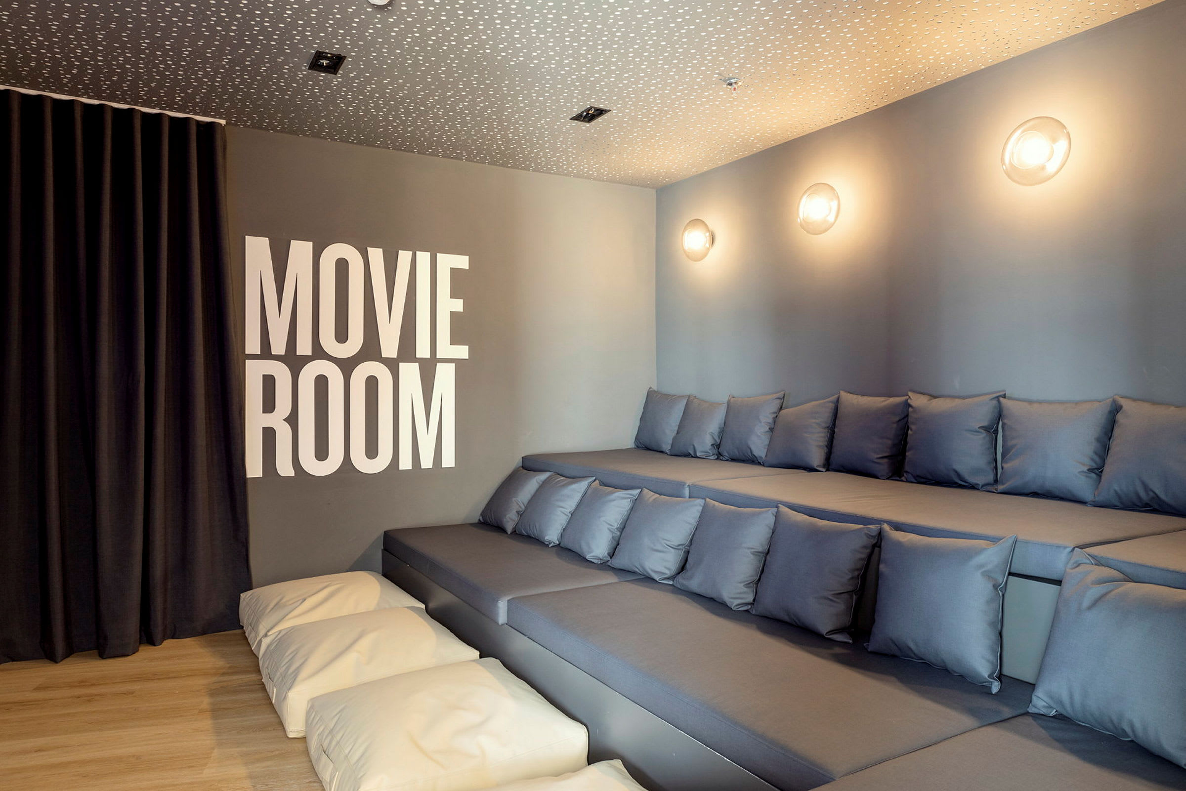 Kuva elokuvahuoneesta, jossa on porrastetut istuimet tyynyillä ja seinällä teksti 'Movie Room'. (Tekoälyn luoma teksti)
