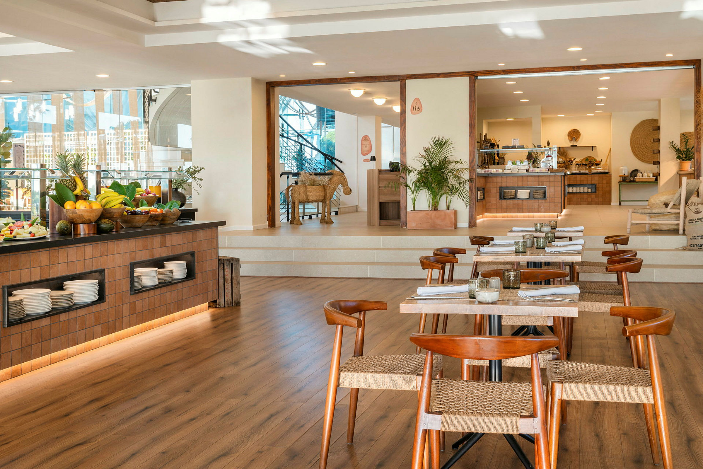 Ravintola, jossa on puupöytiä ja tuoleja sekä hedelmien ja tarjoiluastioiden buffet. (Tekoälyn luoma teksti)