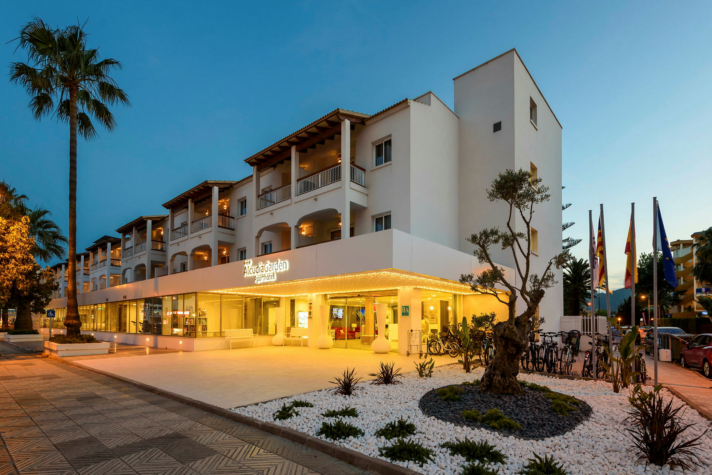Kuva Alcudia Garden Aparthotel -hotellista, valaistu sisäänkäynti ja ympäröivä puutarha. (Tekoälyn luoma teksti)