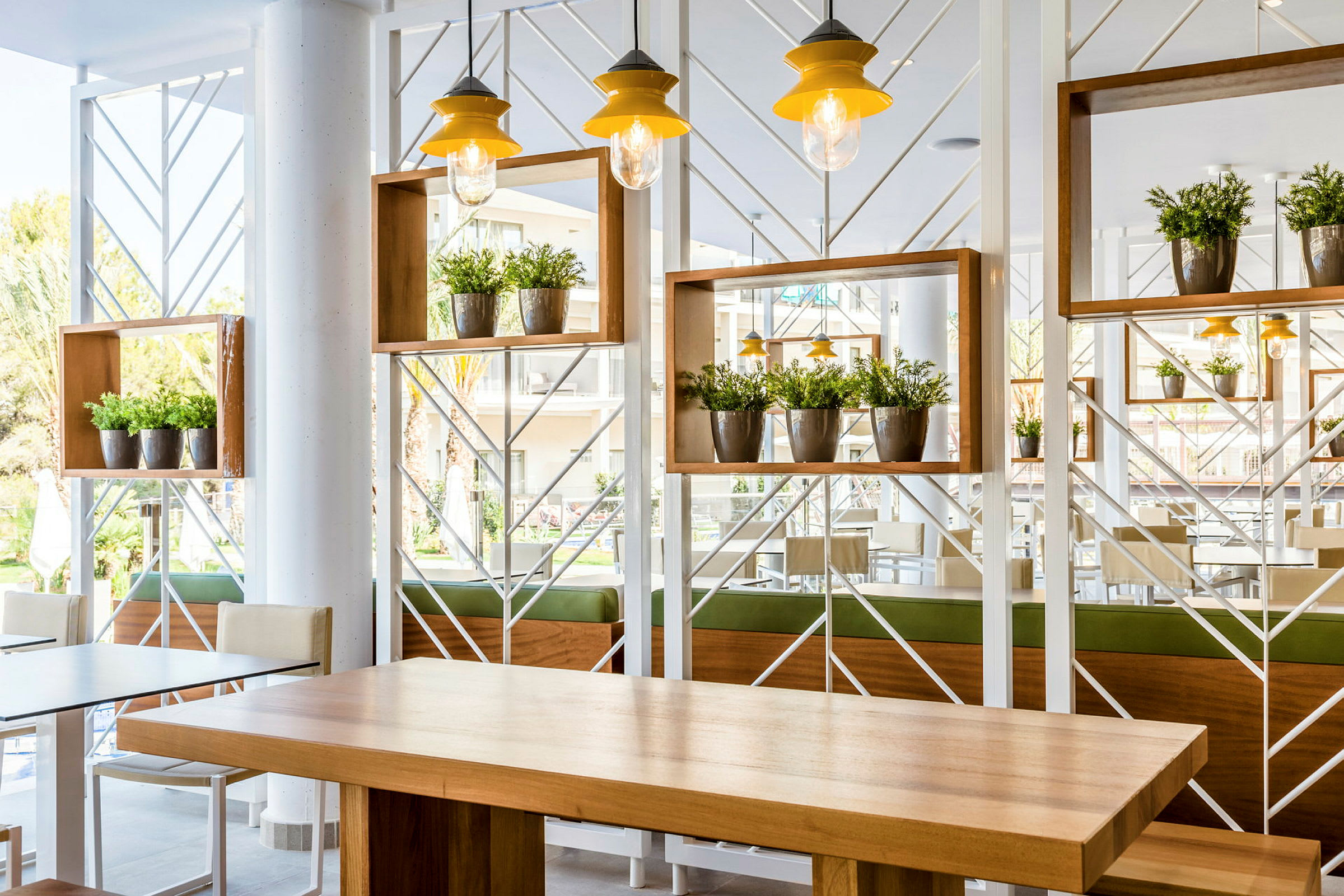 Vaalea ja modernisti sisustettu tila, jossa pöytiä ja kasvikoristeita. (Tekoälyn luoma teksti)