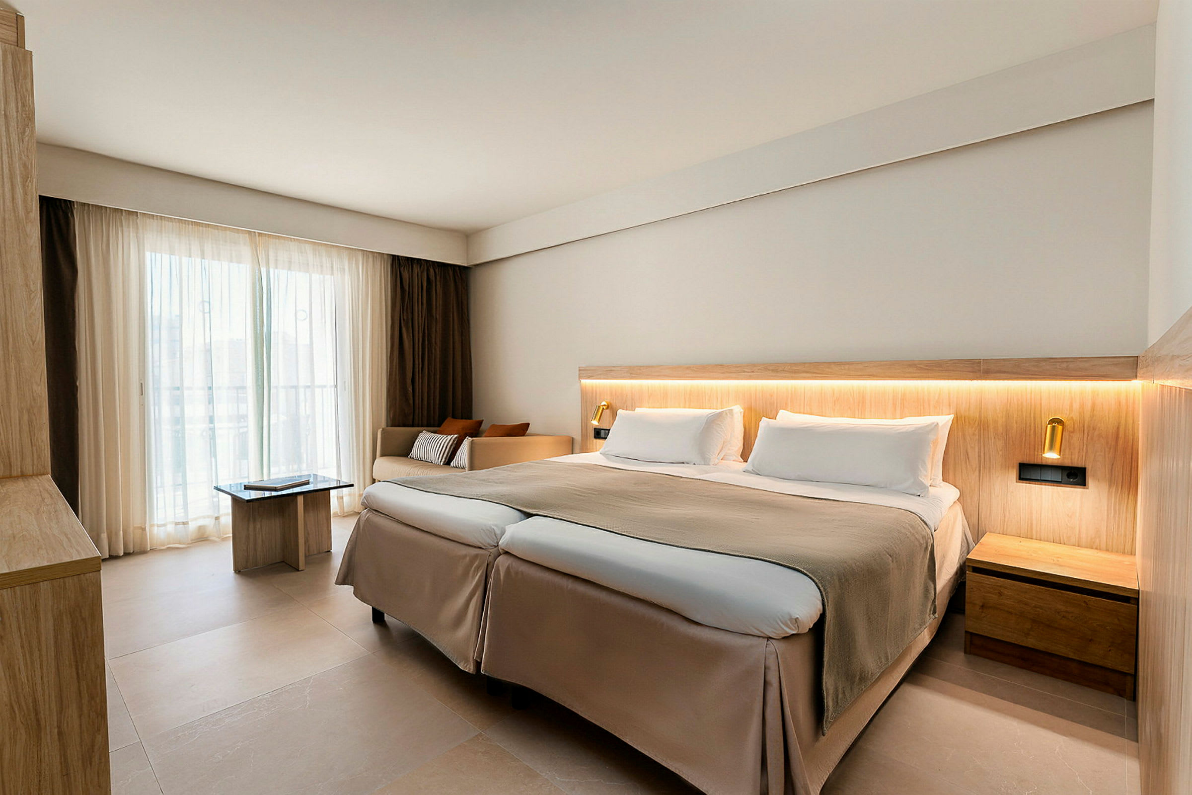 Moderni hotellihuone, jossa on parivuode, vaaleita sävyjä ja isot ikkunat verhoilla. (Tekoälyn luoma teksti)