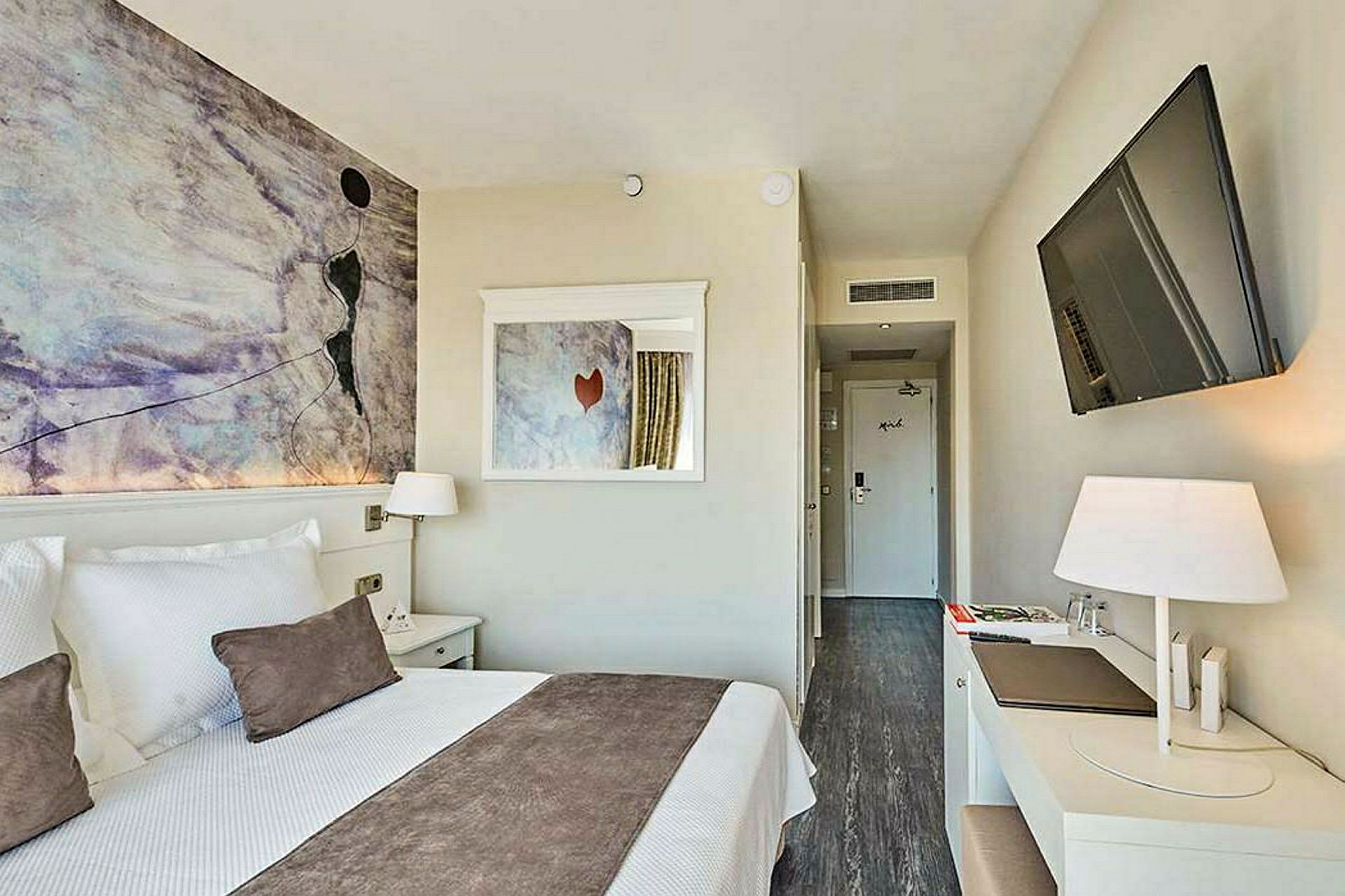 Moderni hotellihuone, jossa on parisänky, seinätaidetta, kirjoituspöytä ja taulutelevisio. (Tekoälyn luoma teksti)