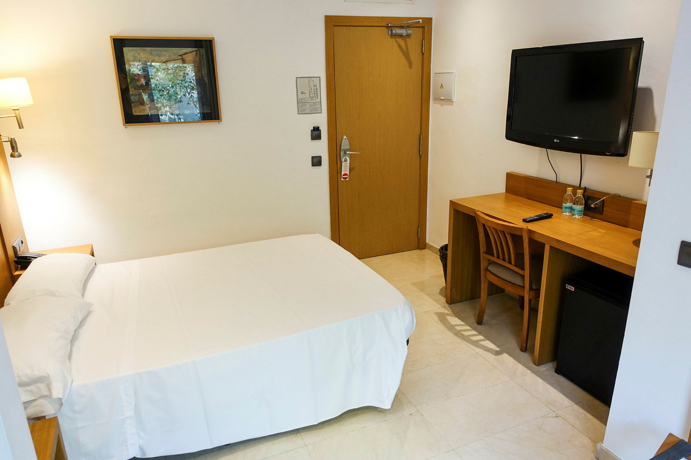 Yksinkertainen hotellihuone, jossa on sänky, kirjoituspöytä ja tuoli. Seinällä on televisio ja taideteos. (Tekoälyn luoma teksti)