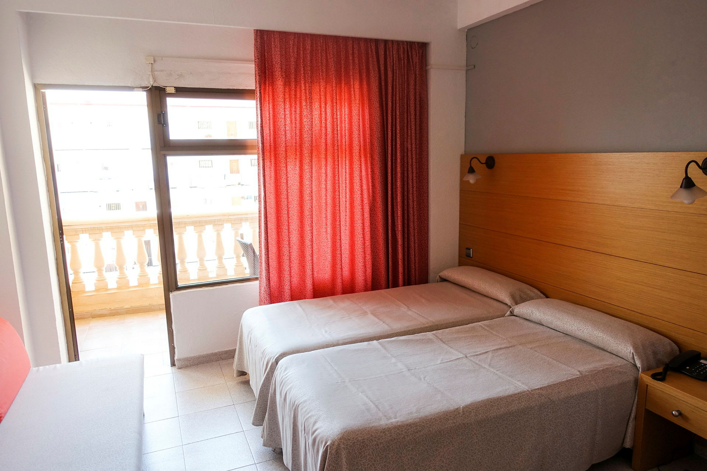 Hotellihuone, jossa kaksi erillistä vuodetta, punainen verho ja parveke. (Tekoälyn luoma teksti)