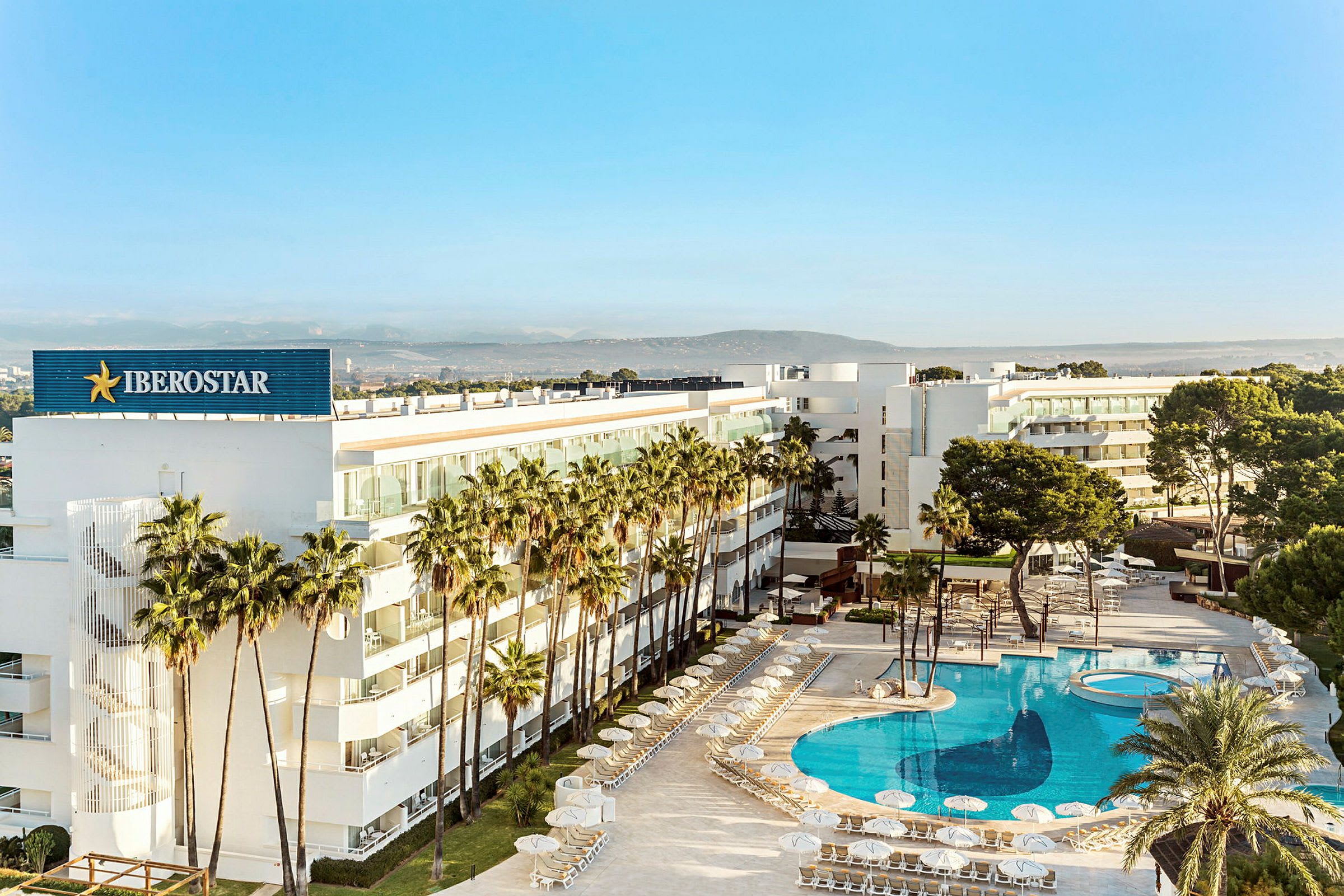 Moderni hotelli palmujen ympäröimänä, jossa on suuri, kirkkaansininen uima-allas. (Tekoälyn luoma teksti)