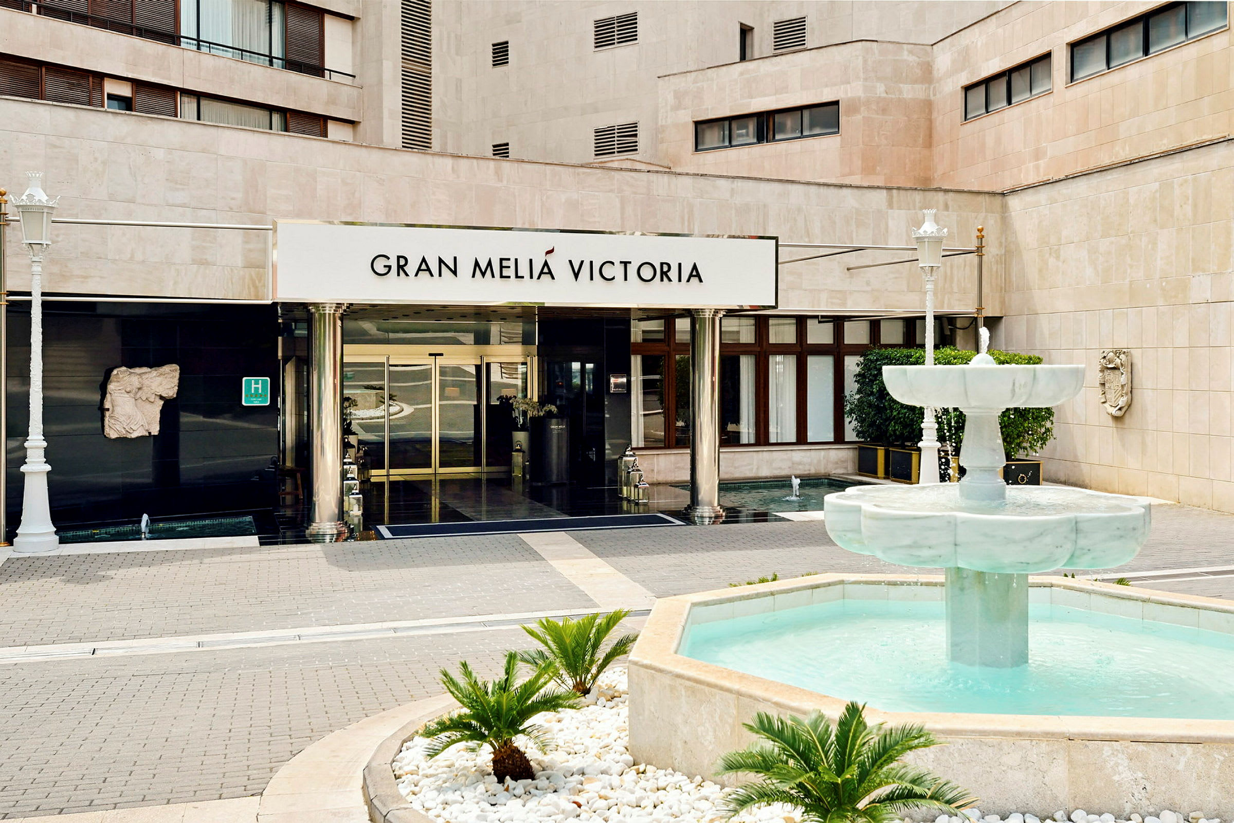 Rakennuksen sisäänkäynti, jonka yläpuolella lukee "Gran Meliá Victoria", sekä edessä kirkasvetinen suihkulähde. (Tekoälyn luoma teksti)