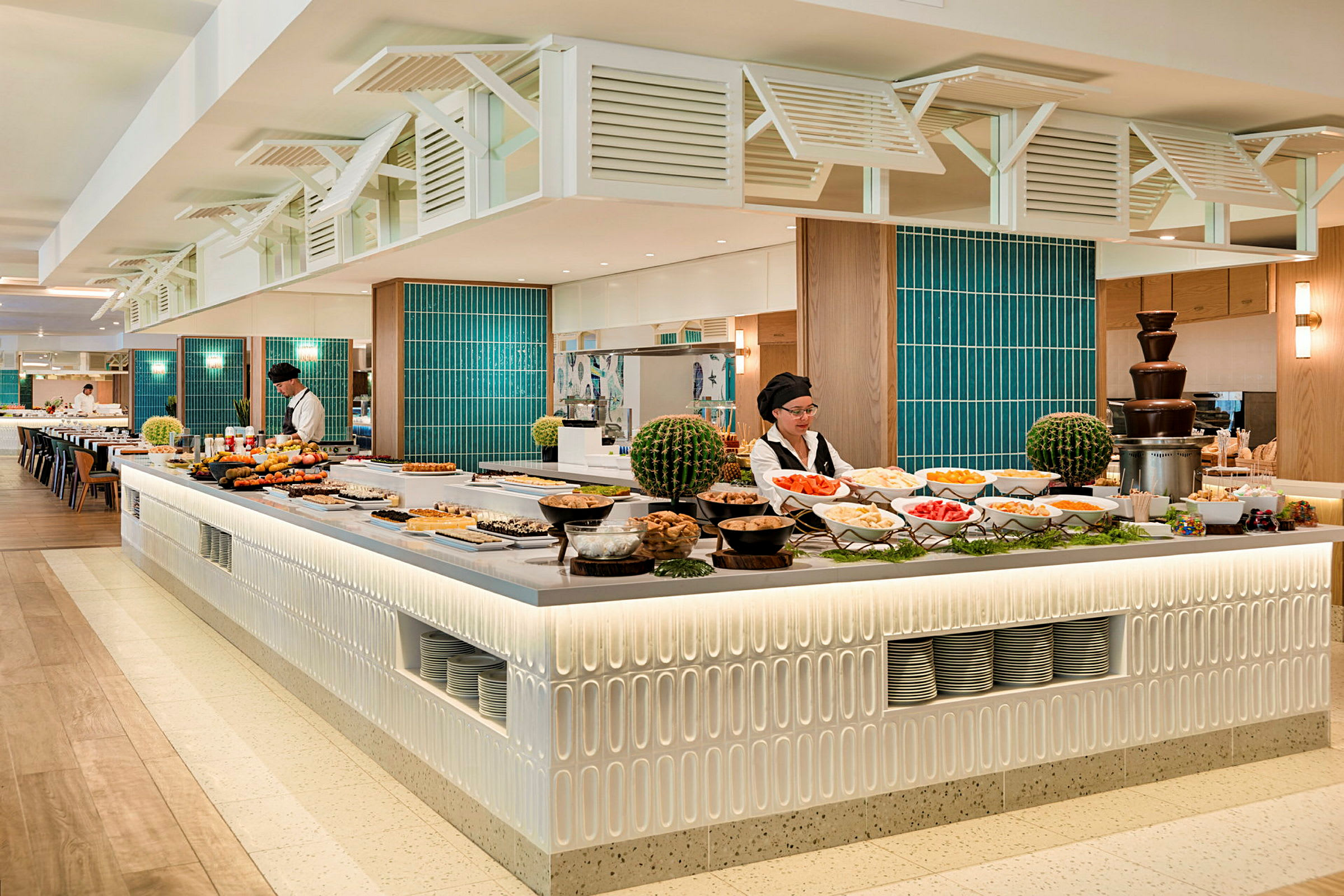 Moderni buffet-tarjoilu, jossa pöydillä on tarjottimille asetettuja ruokia ja lisukkeita. Henkilökunta valmistautuu tarjoiluun. (Tekoälyn luoma teksti)
