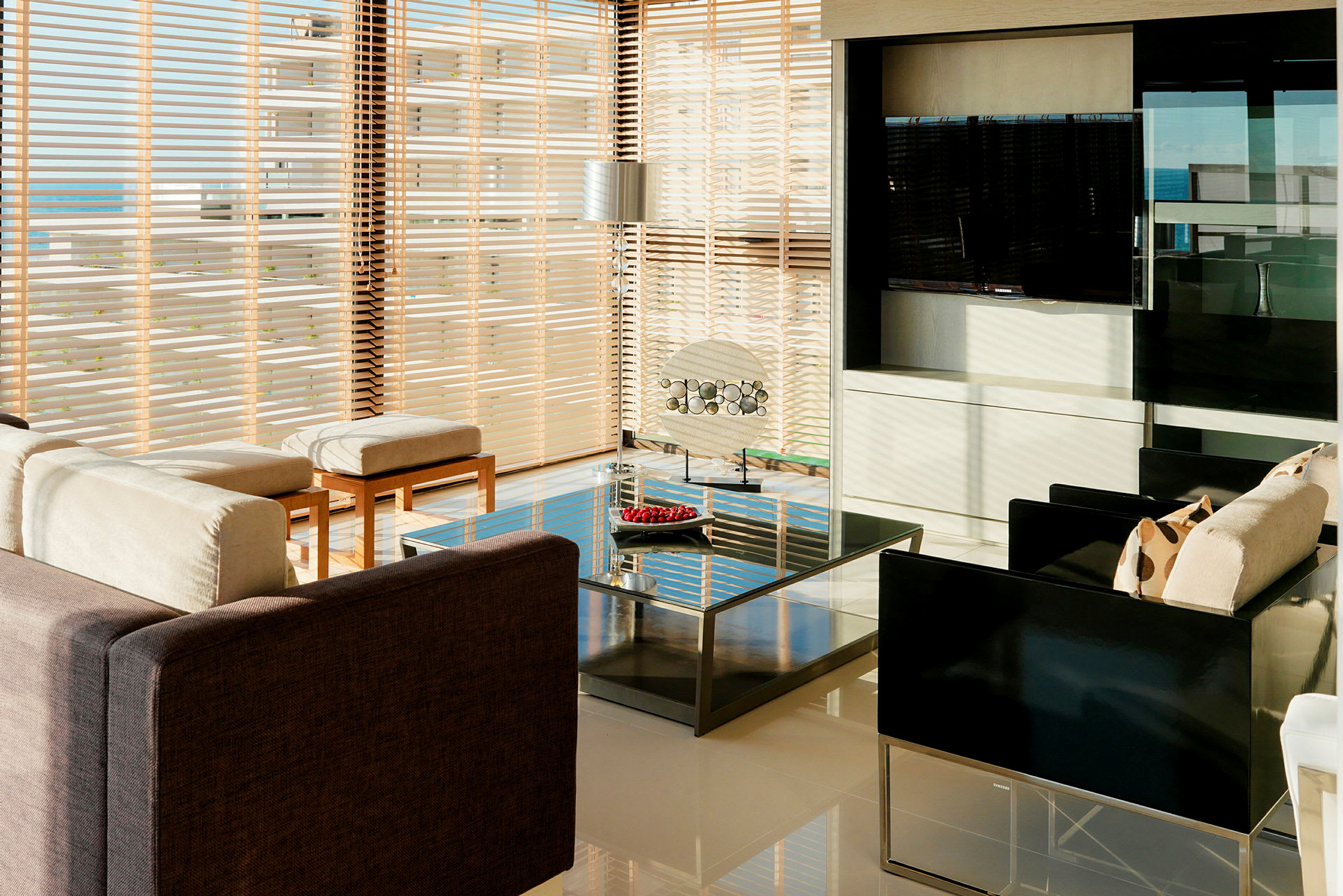 Olohuone modernilla sisustuksella, suuret ikkunat sälekaihtimilla, sohvat, pöytä ja koristeellinen valaistus. (Tekoälyn luoma teksti)