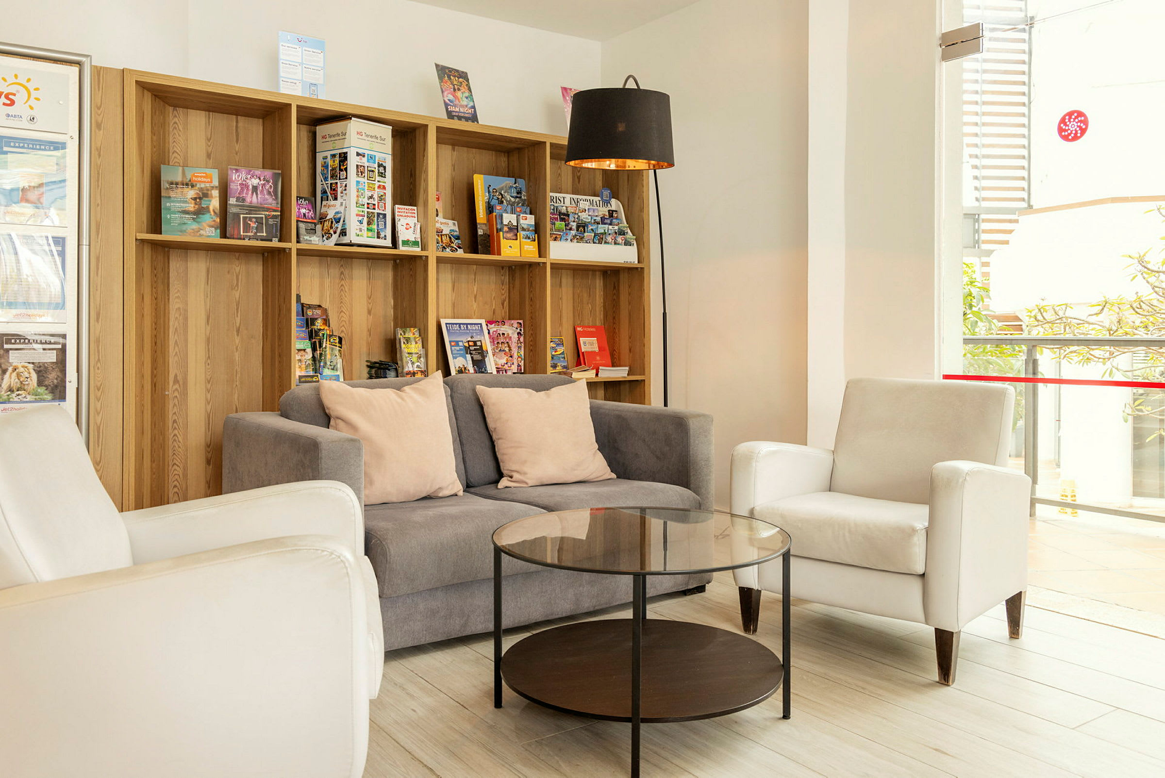 Lounge, jossa on sohva, nojatuolit ja sohvapöytä hyllykkö täynnä esitteitä. (Tekoälyn luoma teksti)