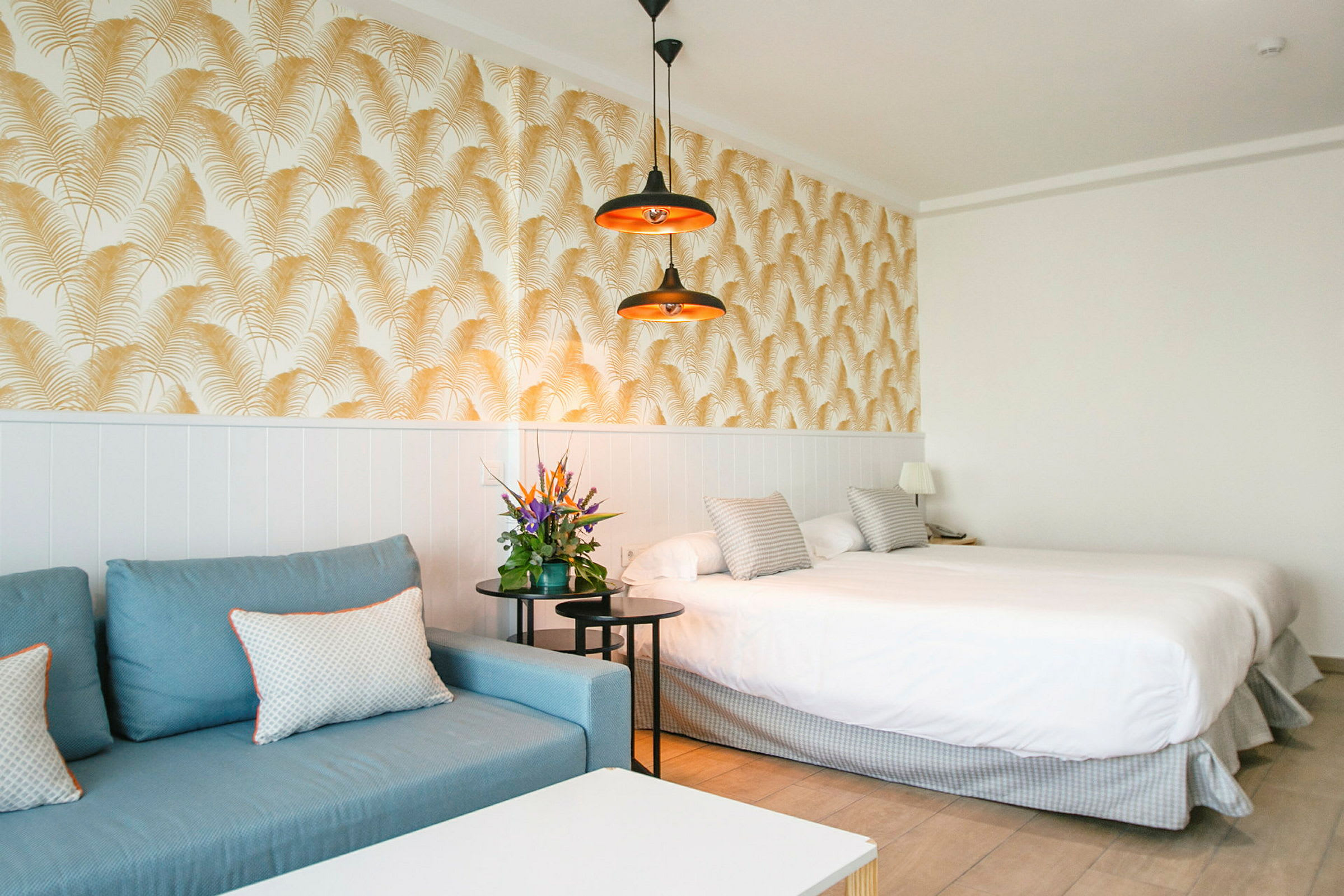 Hotellihuone, jossa sininen sohva, parivuode ja koristeellinen tapetti. (Tekoälyn luoma teksti)