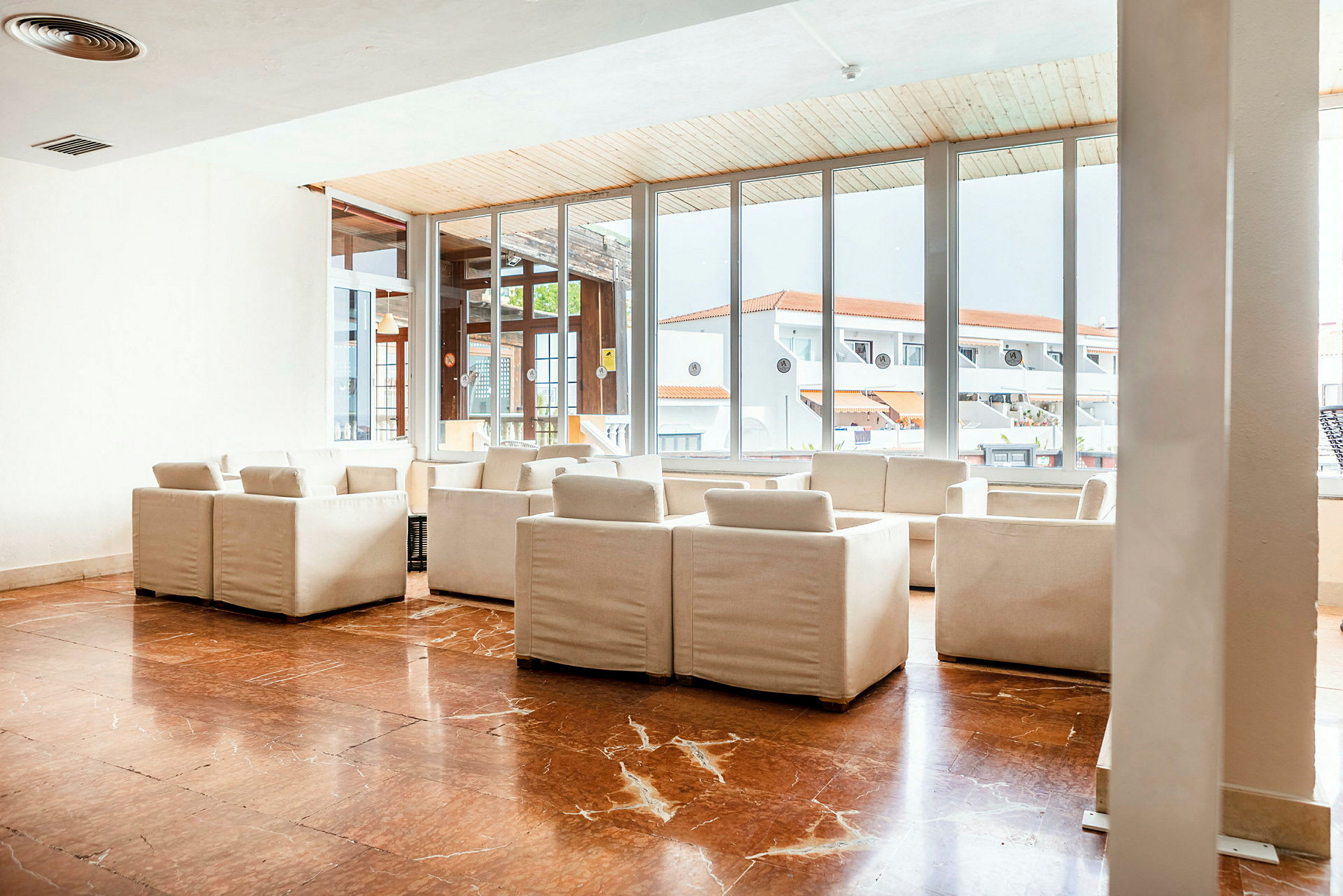 Valoisa lounge, jossa valkoisia sohvia ja tuoleja, marmorilattia ja suuret ikkunat, joista näkymät ympäröiviin punakattoisiin rakennuksiin. (Tekoälyn luoma teksti)
