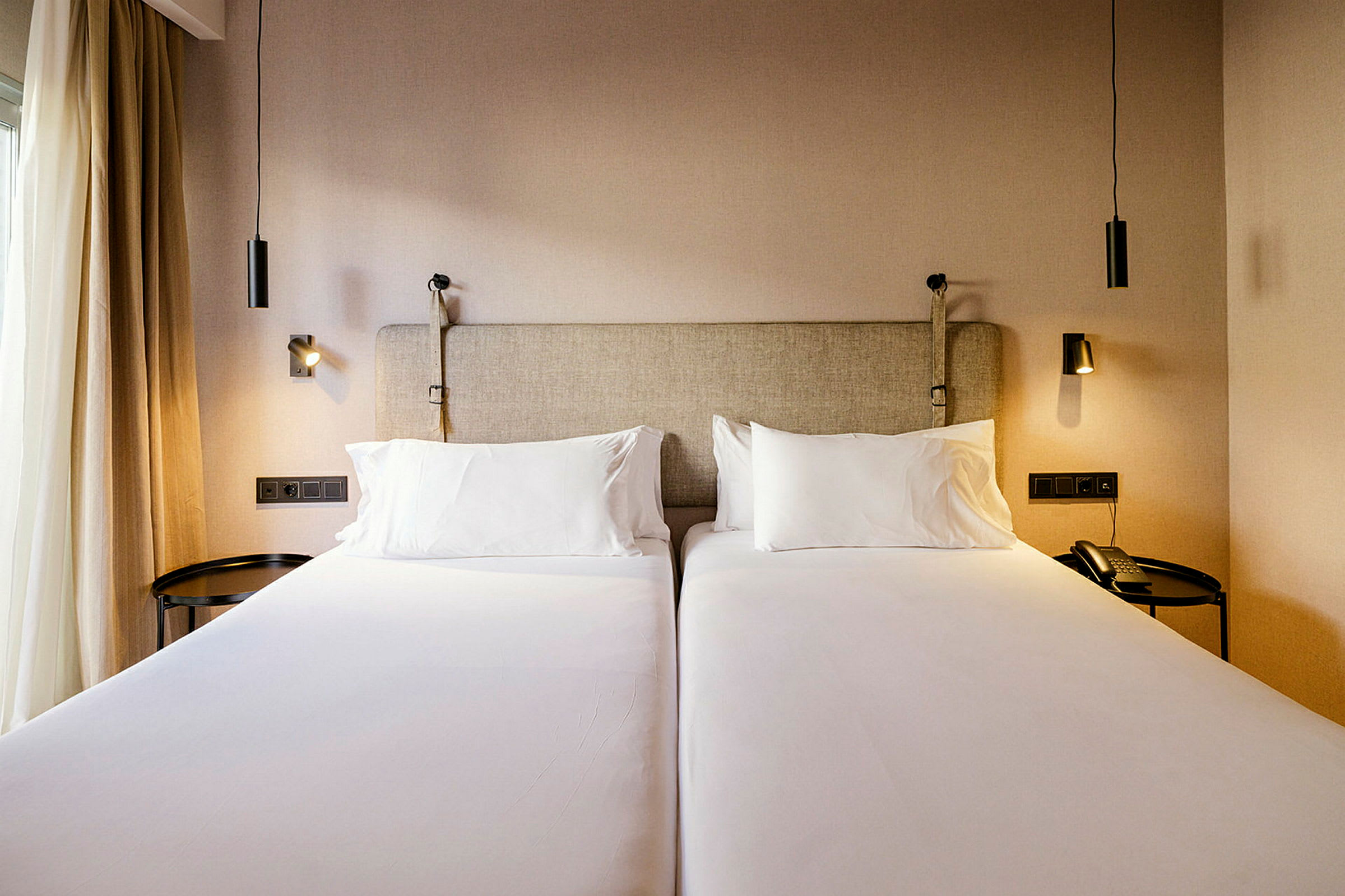 Kaksi yhden hengen sänkyä hotellihuoneessa, joissa sängynvalot. (Tekoälyn luoma teksti)