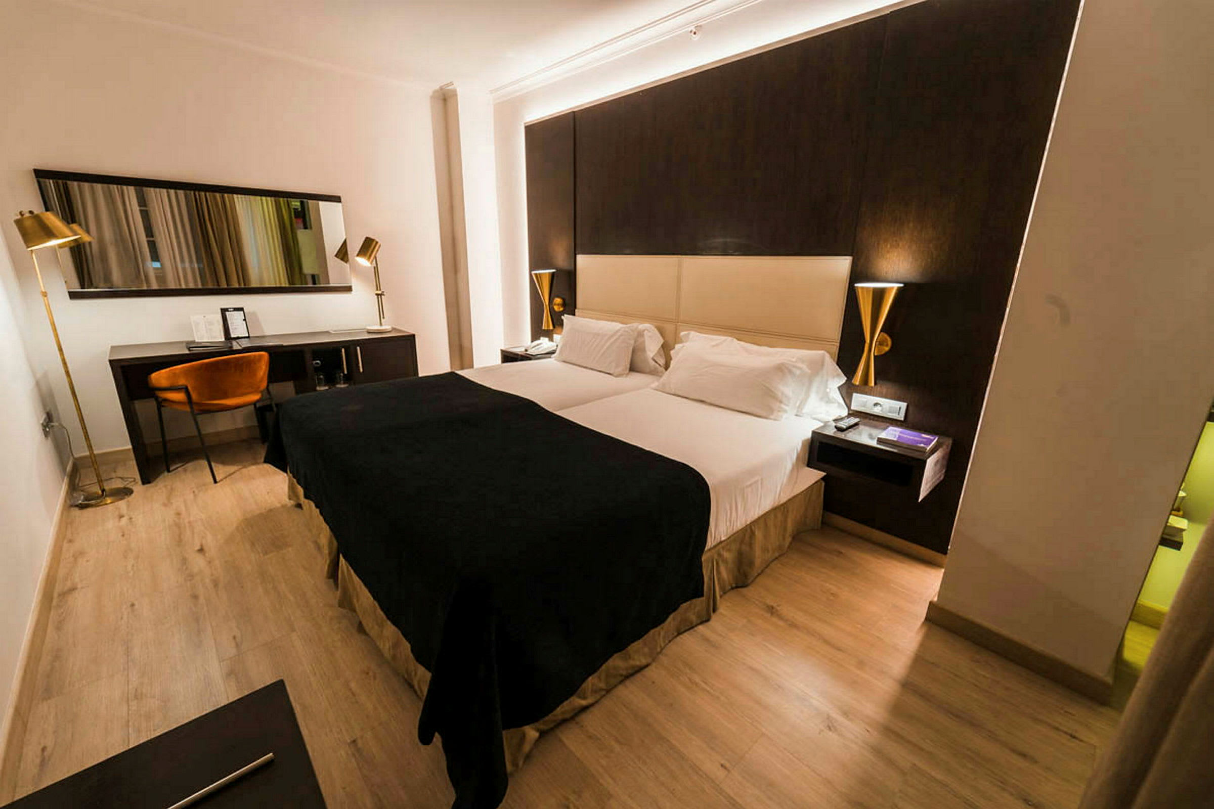 Hotellihuone, jossa on parisänky, tumma ja vaalea värisävy huonekaluissa sekä työpiste tuolin ja peilin kanssa. (Tekoälyn luoma teksti)