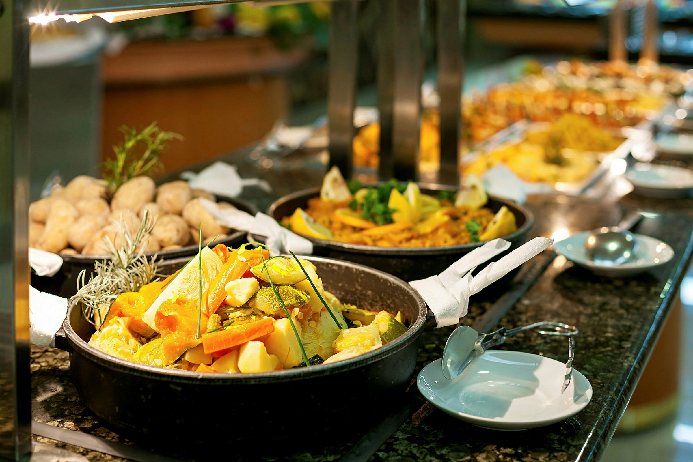 Buffet, jossa on erilaisia ruokia, mukaan lukien vihanneksia padassa ja paistettuja perunoita. (Tekoälyn luoma teksti)