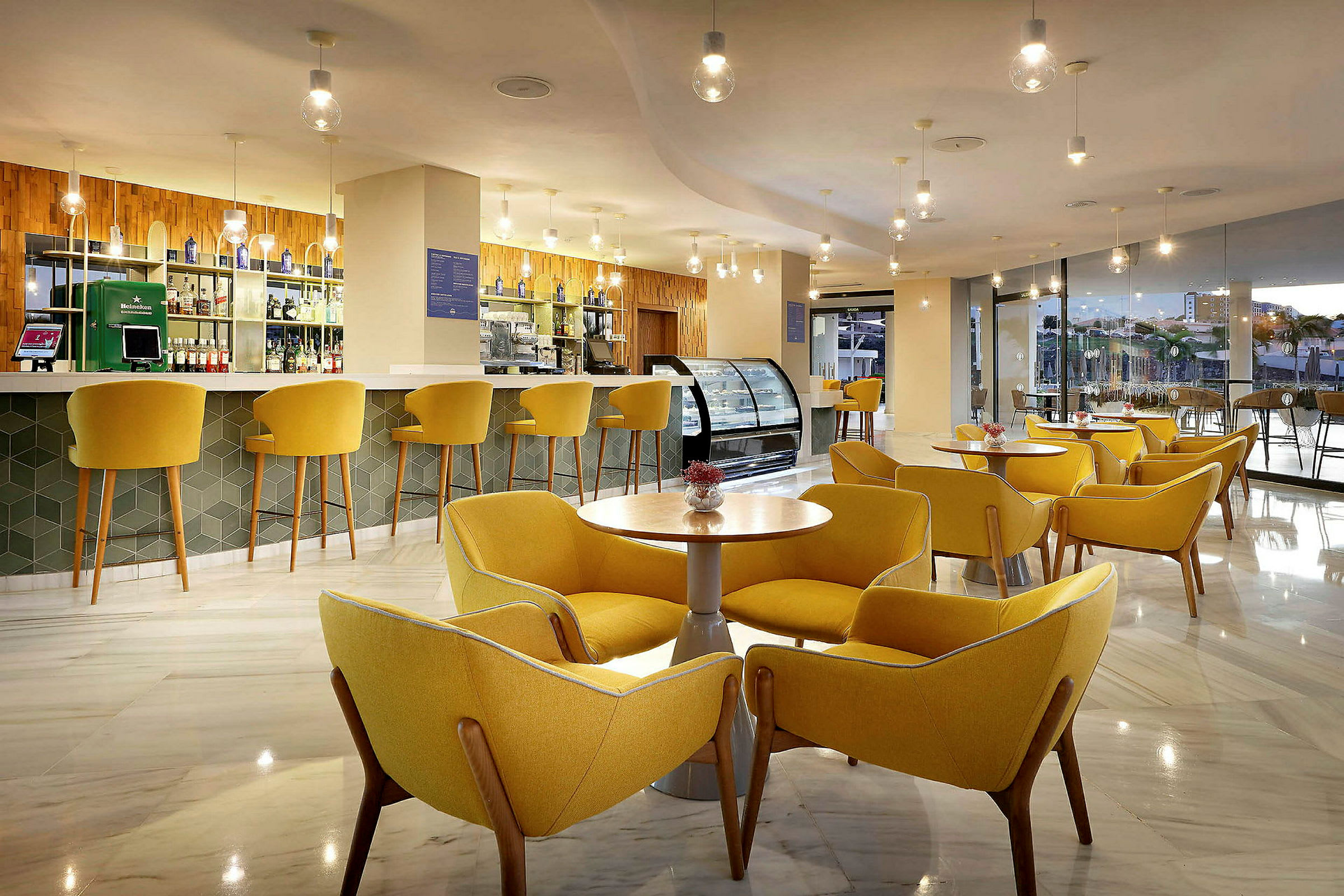 Moderni lounge, jossa on keltaisia tuoleja ja pöytiä sekä taustalla baari. (Tekoälyn luoma teksti)