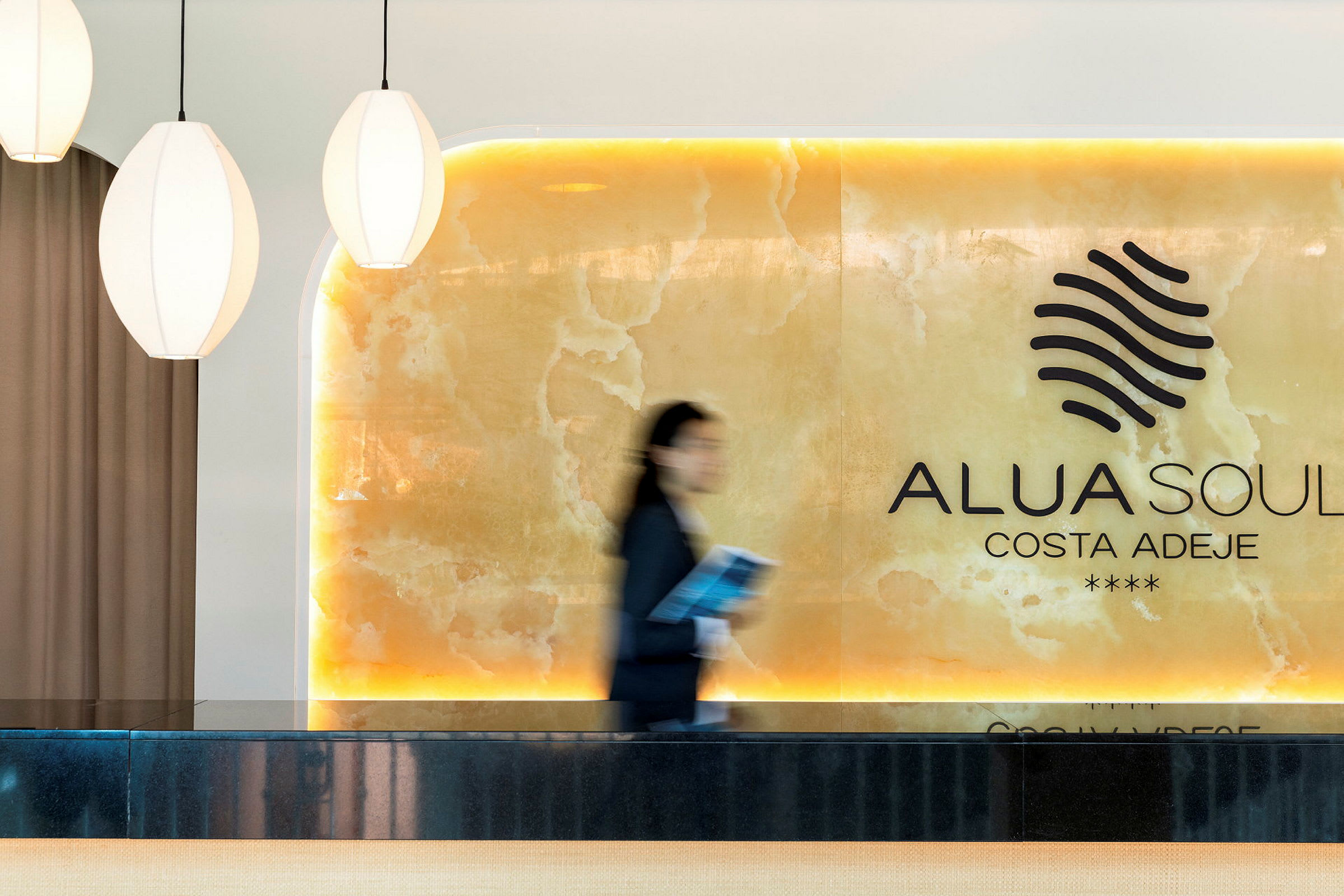 Alua Soul Costa Adeje -hotellin vastaanotto, jossa on vaaleita yksityiskohtia ja liikkuva henkilö. (Tekoälyn luoma teksti)