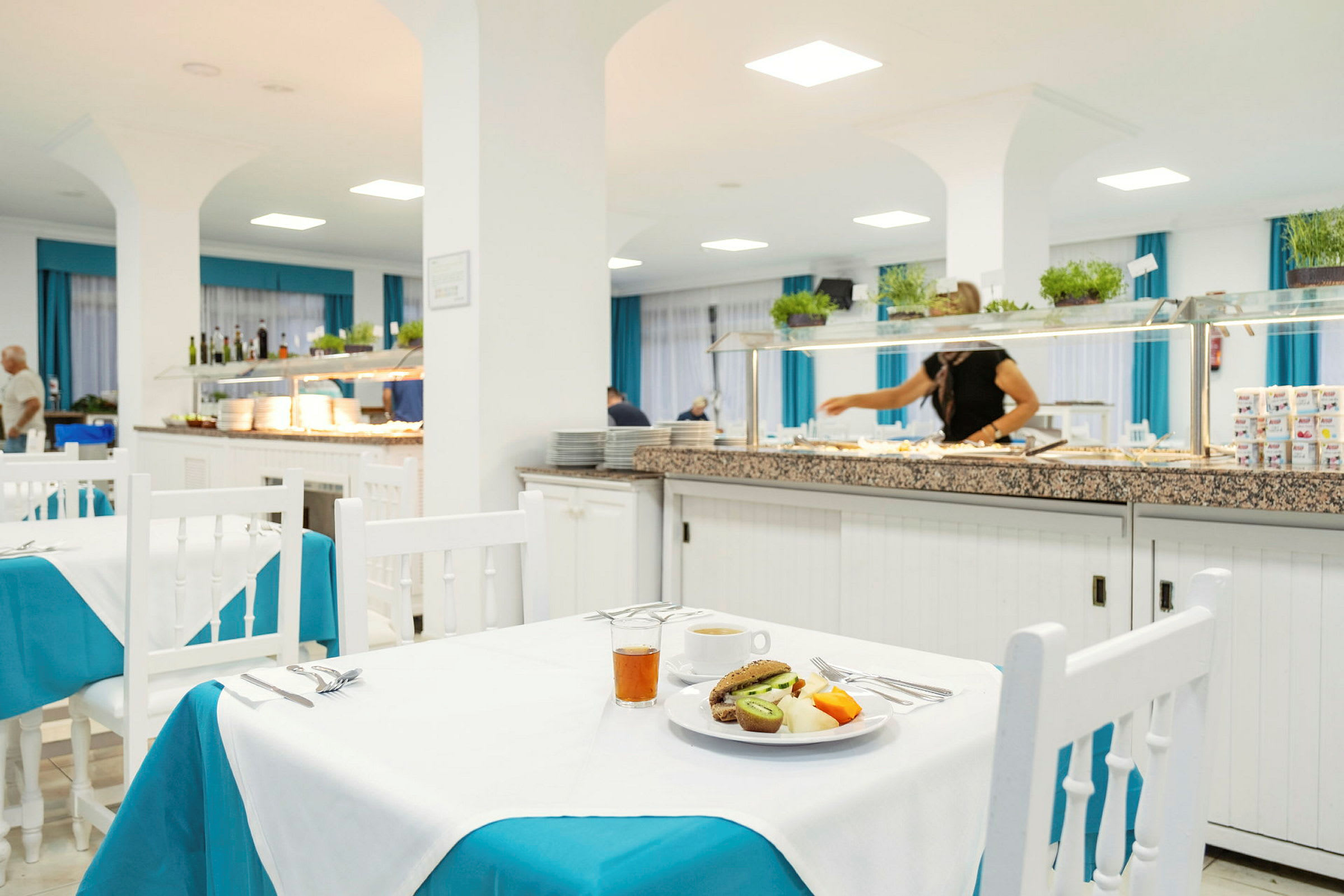 Ruokailutila, jossa katettuja pöytiä ja buffetalue taustalla. (Tekoälyn luoma teksti)