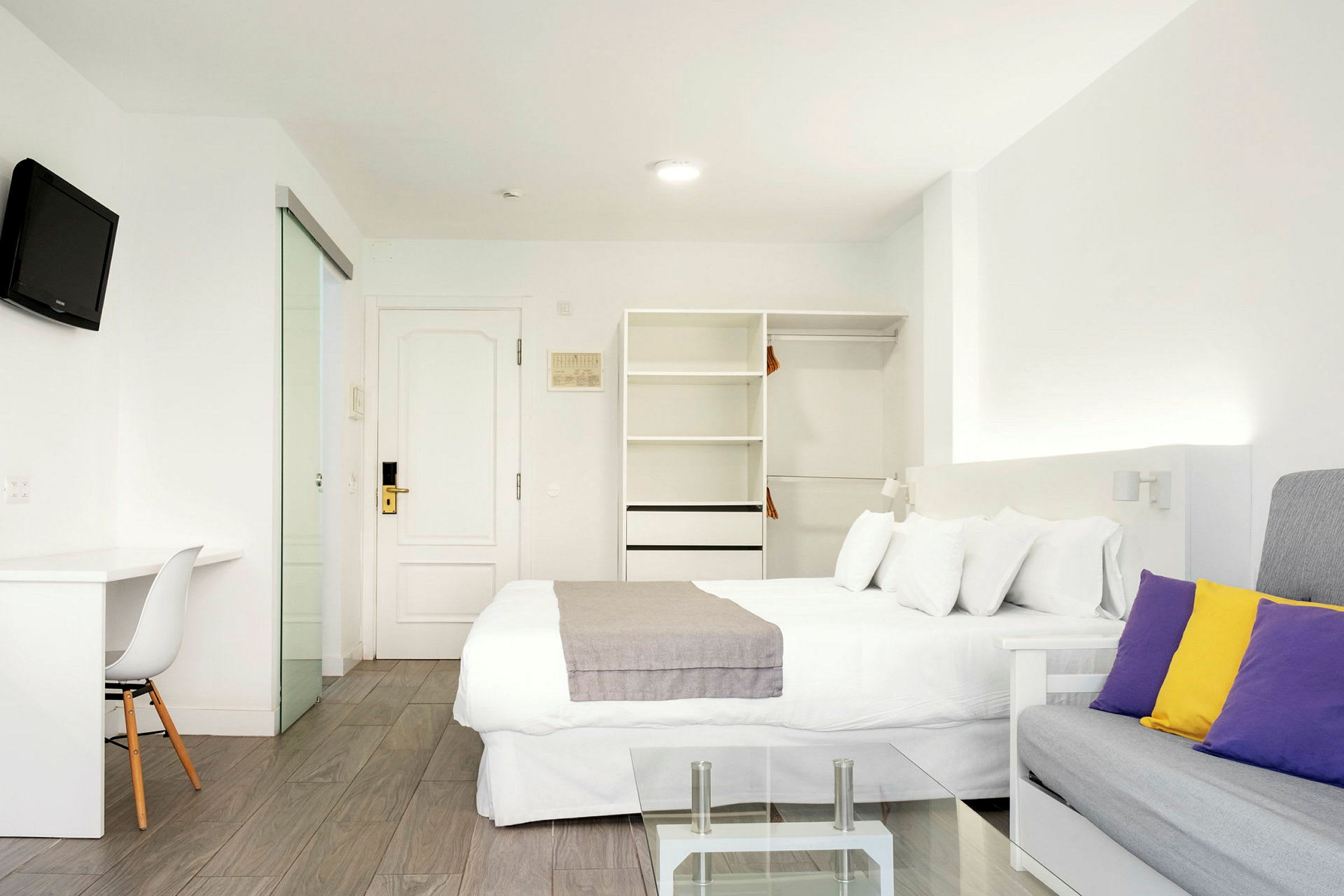 Moderni hotellihuone, jossa valkoinen sisustus ja värikkäitä tyynyjä. (Tekoälyn luoma teksti)