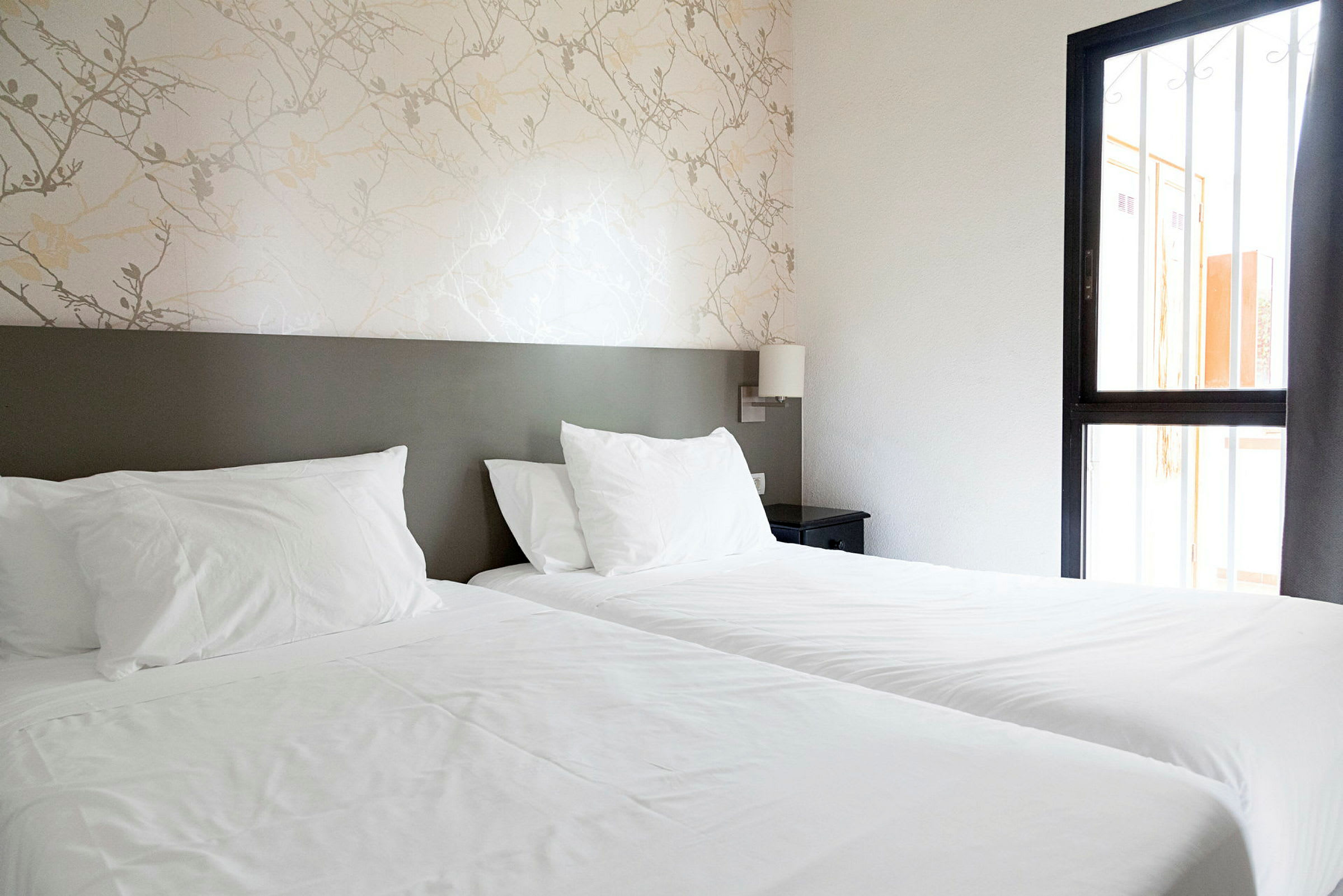 Hotellihuone, jossa on kaksi yhden hengen vuodetta ja yöpöytä. (Tekoälyn luoma teksti)