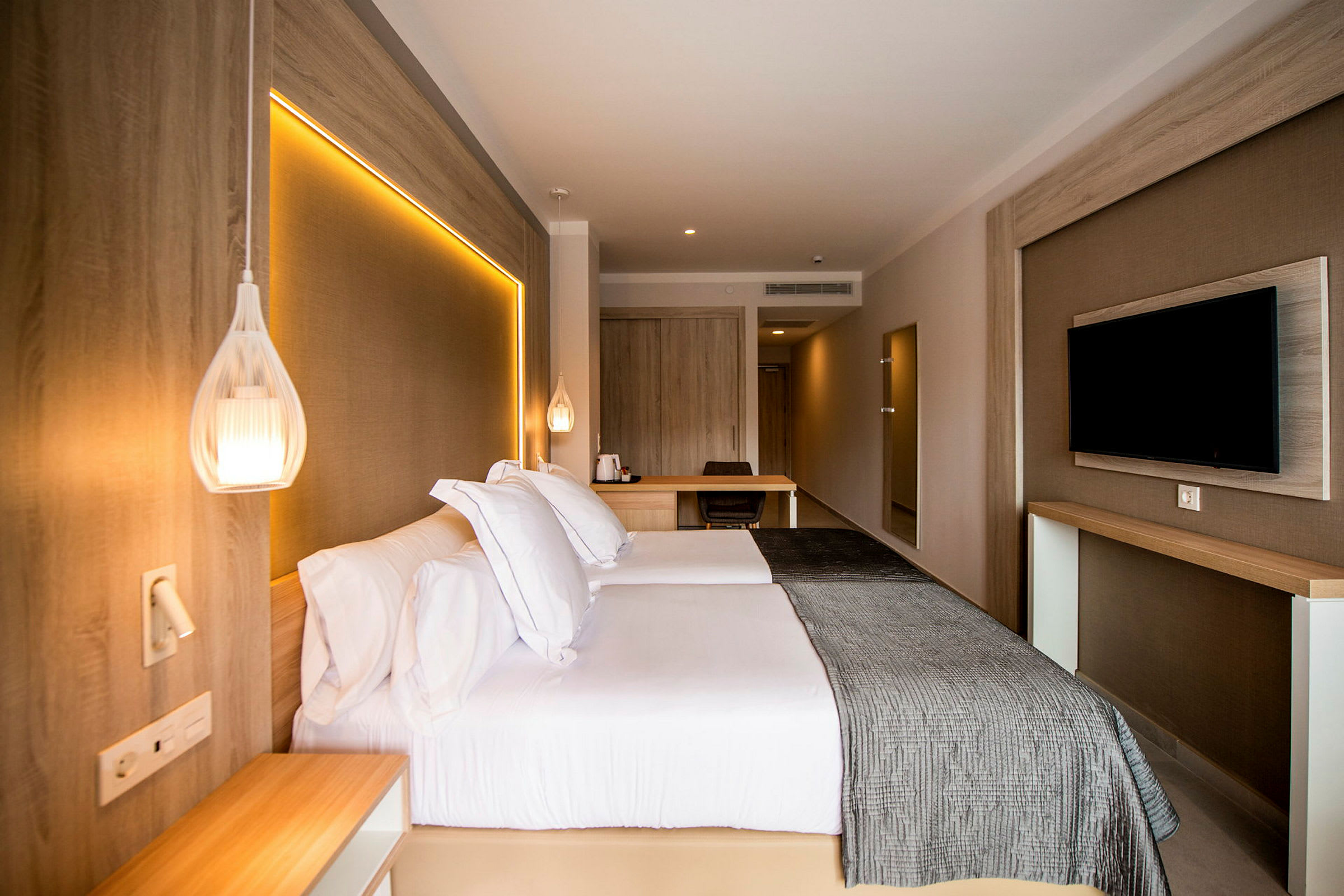 Hotellihuone, jossa parivuode, seinään kiinnitetty televisio ja työpöytä. (Tekoälyn luoma teksti)