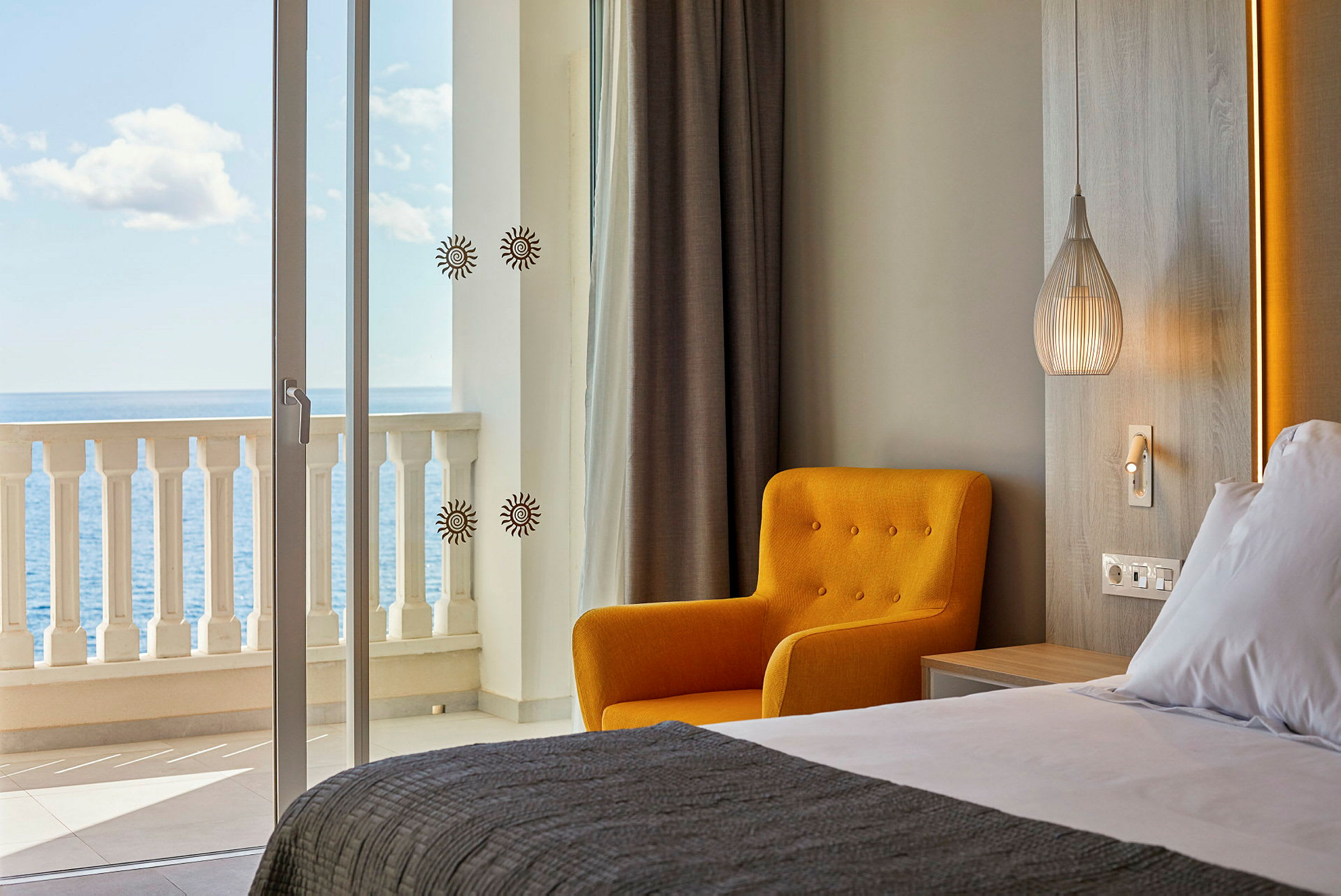 Hotellihuone merinäköalalla. Etualalla näkyy pedattu sänky, keltainen tuoli ja moderni valaisin. (Tekoälyn luoma teksti)
