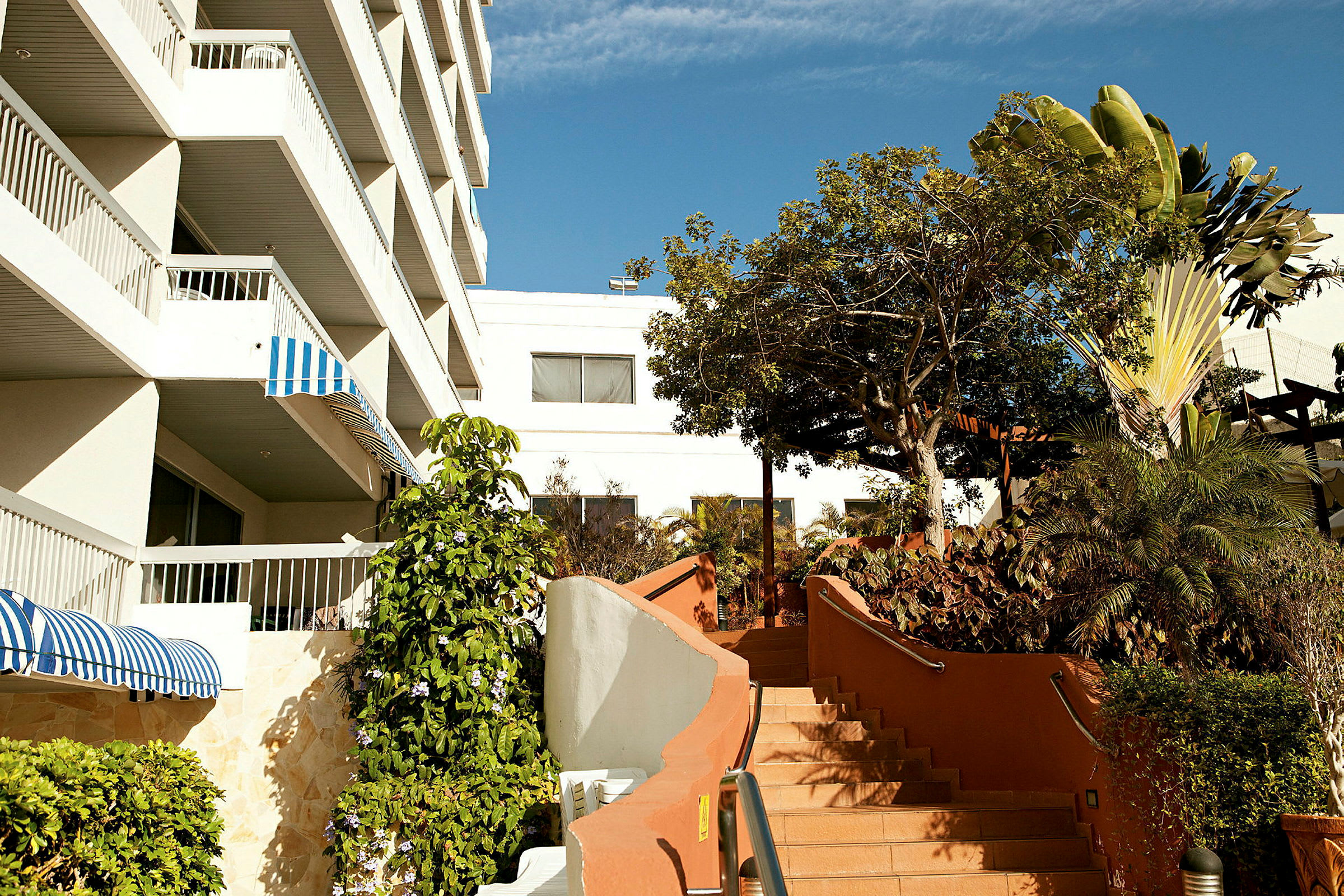 Kuva rakennuksesta, jossa on useita parvekkeita, ja kivinen portaikko, jota ympäröivät vihreät kasvit. (Tekoälyn luoma teksti)