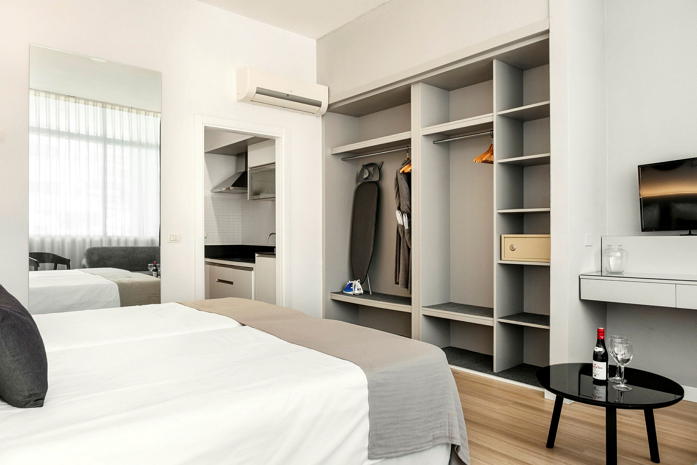 Moderni hotellihuone, jossa on sänky, vaatekaappi, televisio ja keittonurkkaus. (Tekoälyn luoma teksti)