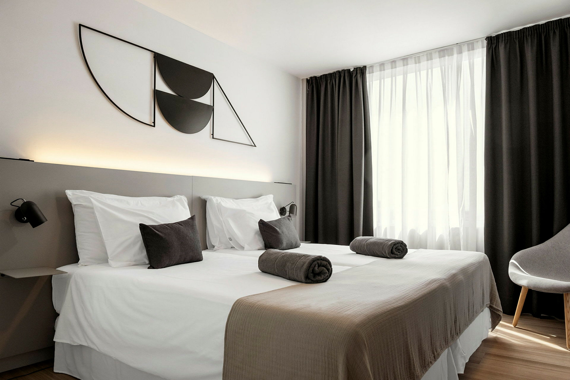 Hotellihuone, jossa on kaksi erillistä vuodetta, tummat verhot ja moderni seinäkoriste. (Tekoälyn luoma teksti)