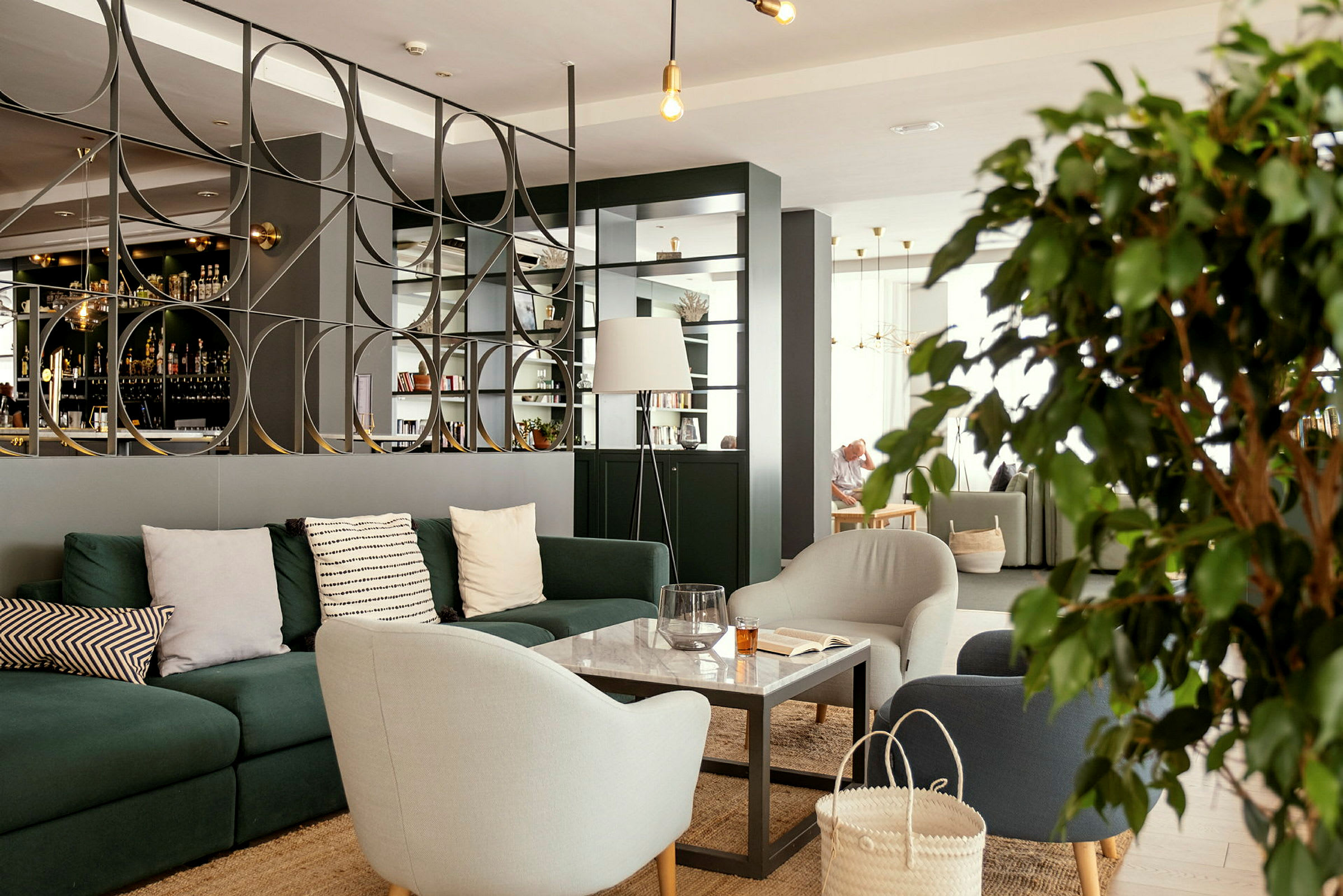 Moderni lounge, jossa sohvia, nojatuoleja ja pöytä koristeellisen tilanjakajan edessä. (Tekoälyn luoma teksti)