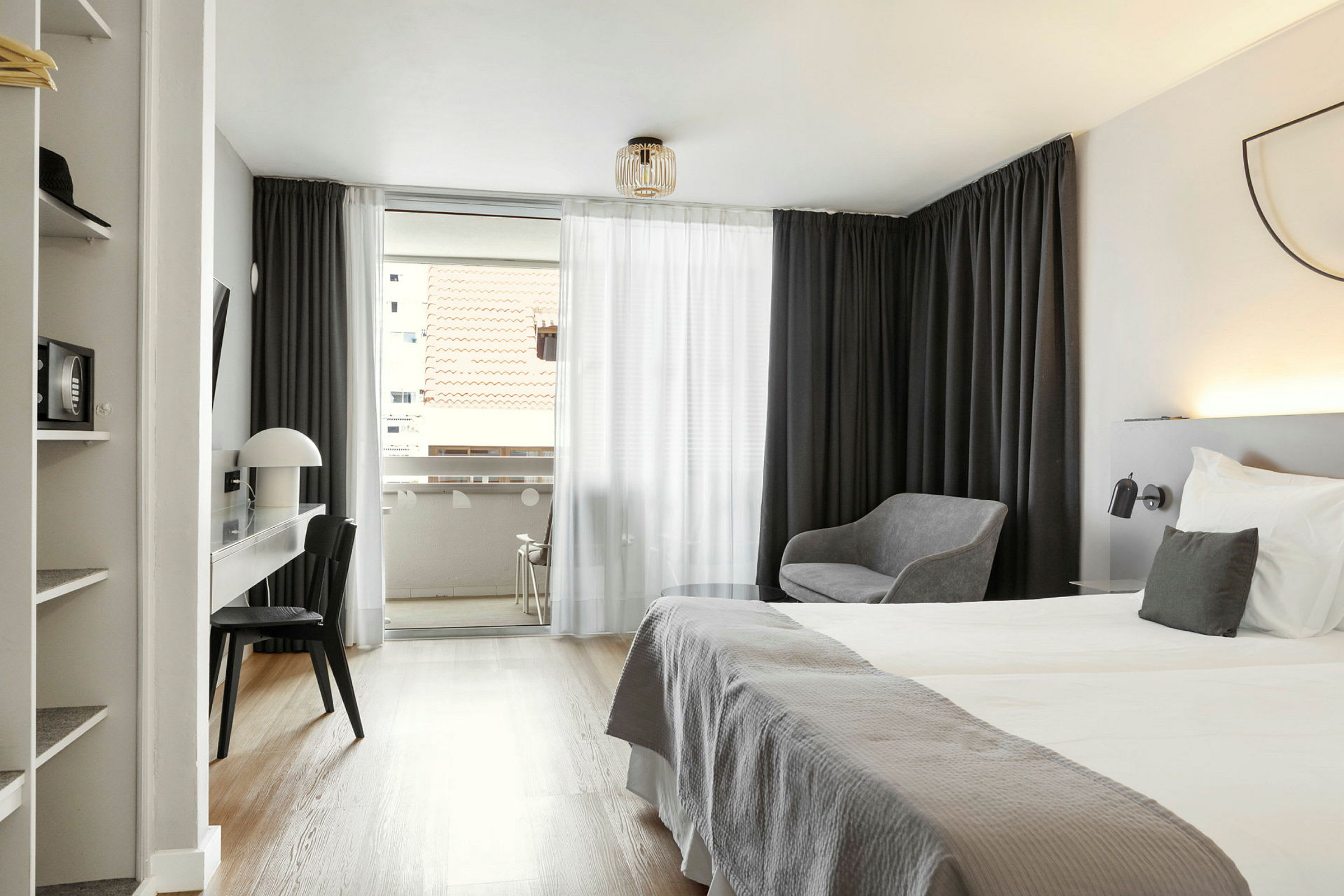 Hotellihuone, jossa parivuode, kirjoituspöytä, tuoli ja oleskelutila; näkymä parvekkeelle, jolta on näkymä katon yli. (Tekoälyn luoma teksti)