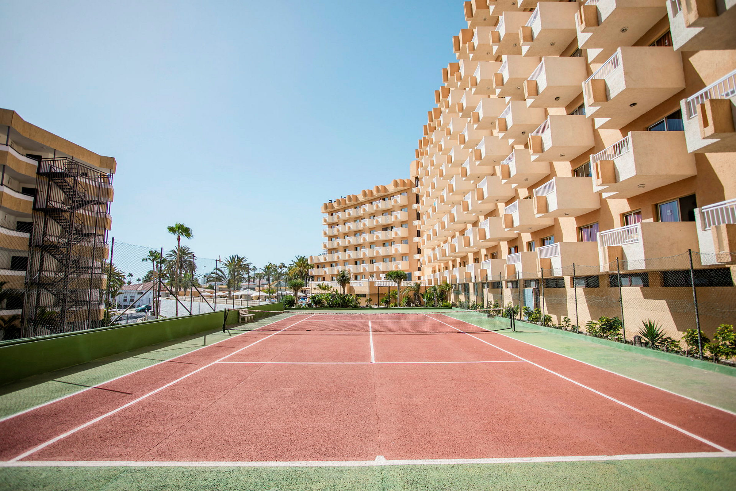 Tenniskenttä hotellirakennuksen edessä jossa parvekkeita. (Tekoälyn luoma teksti)