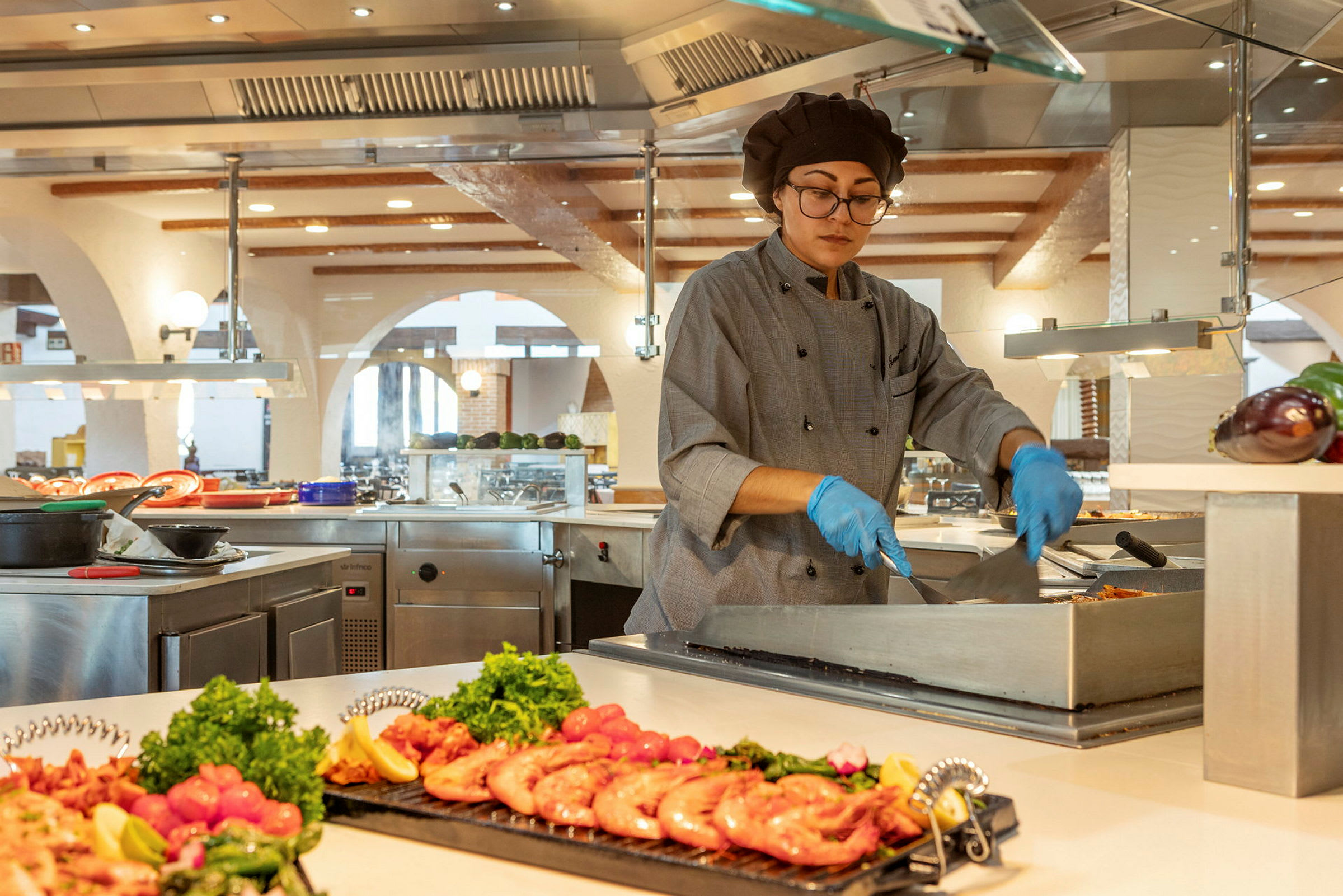 Kokki valmistaa ruokaa buffet-asemalla nykyaikaisessa keittiössä tuoreiden ainesosapinot ympärillään. (Tekoälyn luoma teksti)