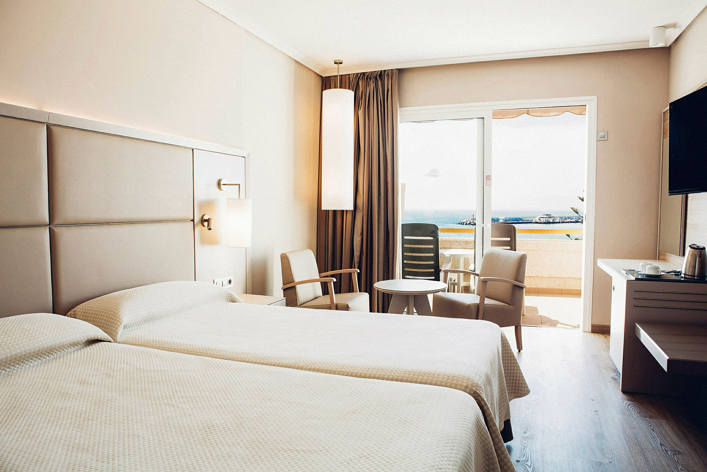 Hotellihuone, jossa kaksi sänkyä, istuinkulmaus ja parveke näkymällä. (Tekoälyn luoma teksti)