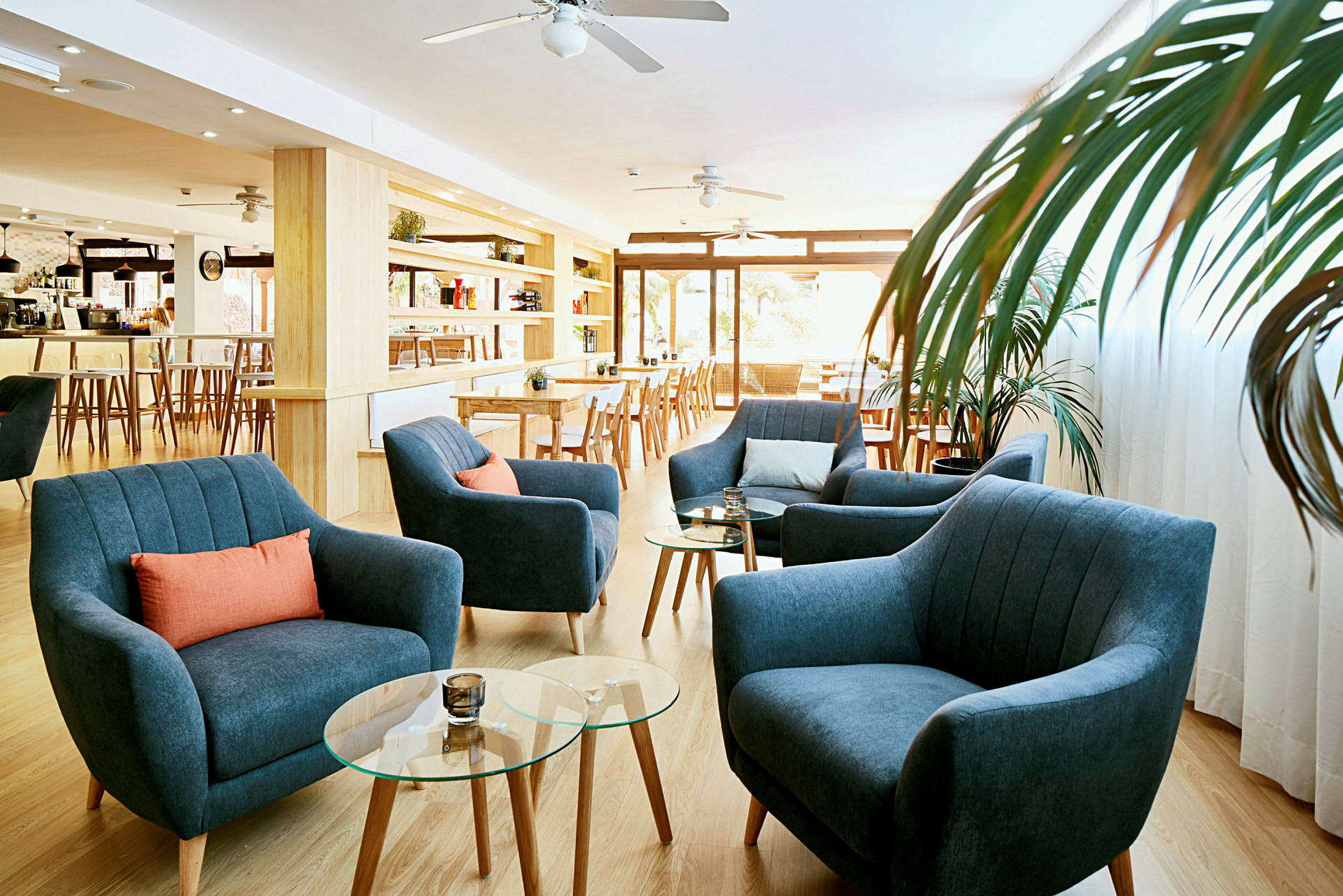 Valoisa lounge-tila, jossa sinisiä nojatuoleja, oransseja tyynyjä ja lasipöytiä. (Tekoälyn luoma teksti)