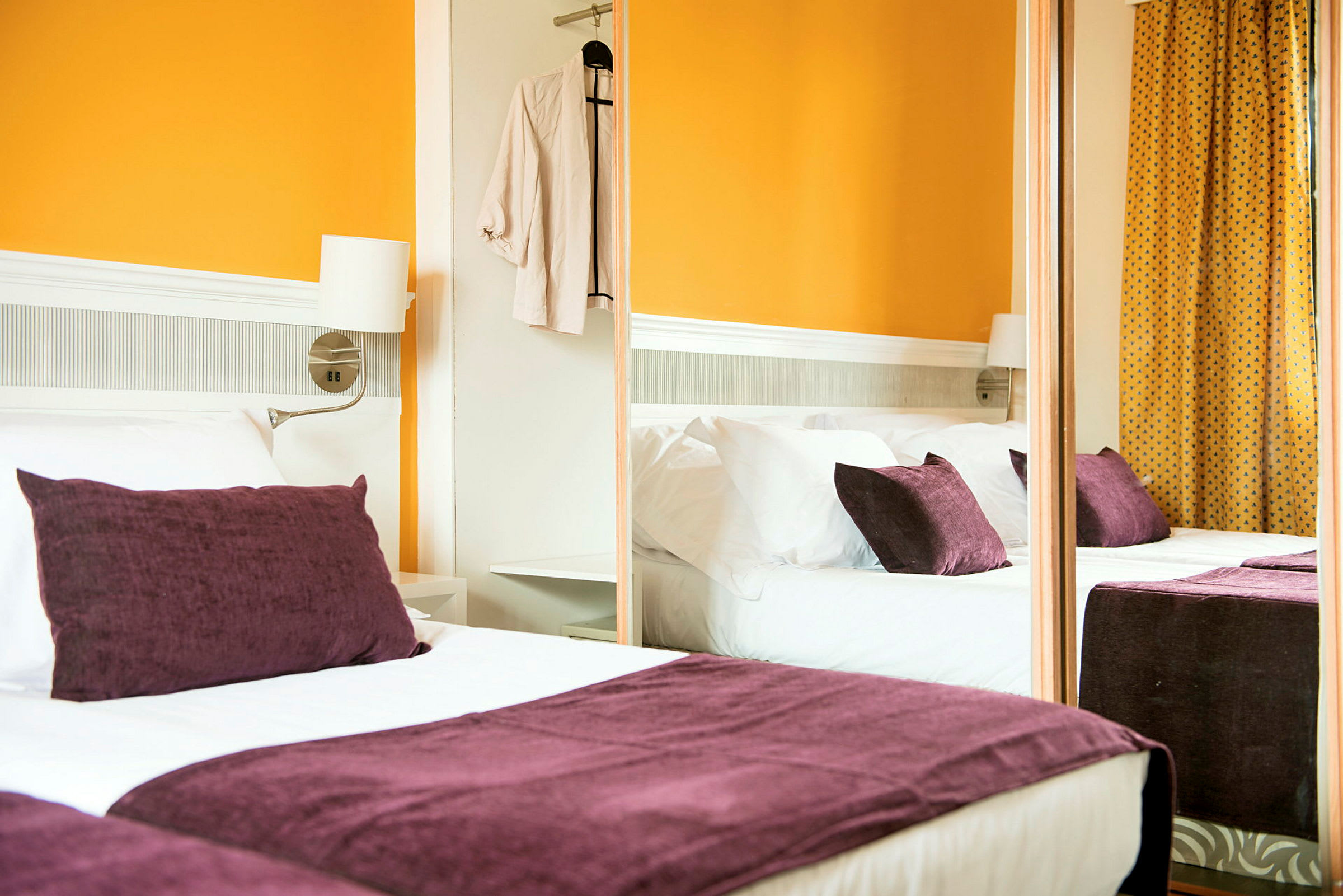 Hotellihuone, jossa on parivuode, violetit tyynyt ja oranssit seinät. (Tekoälyn luoma teksti)