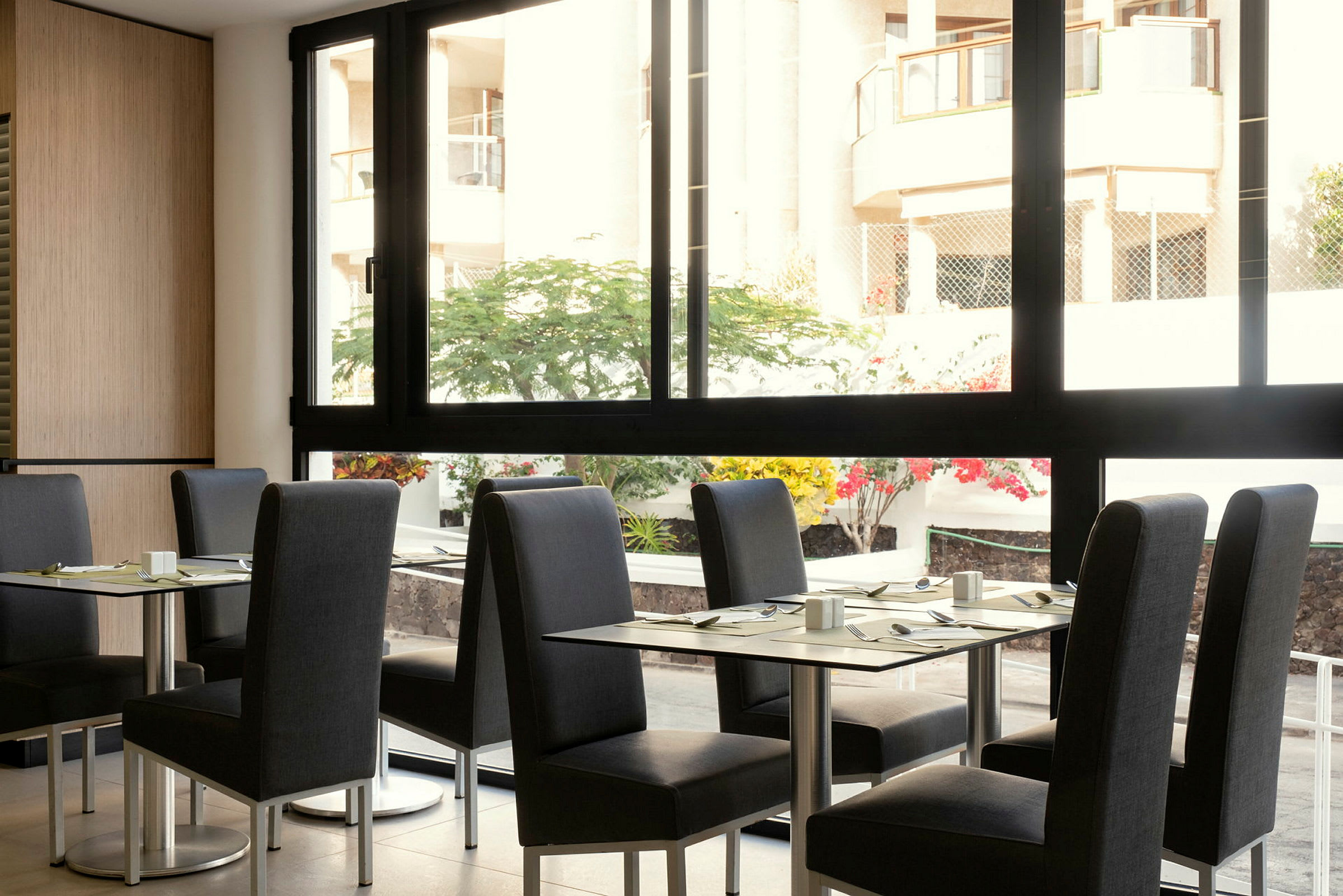 Ravintola, jossa on pöytiä ja tuoleja, ja näkymä sisäpihalle suuren ikkunan kautta. (Tekoälyn luoma teksti)
