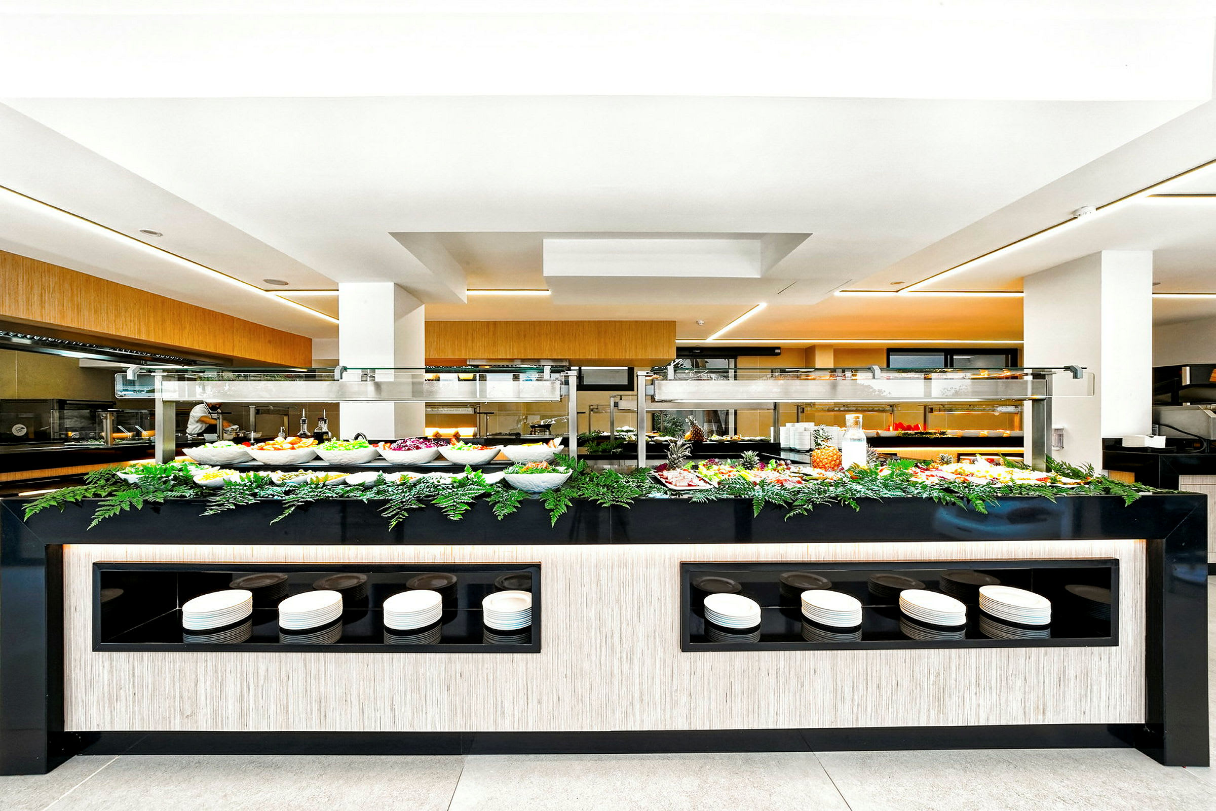 Buffet, jossa on salaattia ja muita ruokia kulhoissa, ympärillä kasveja ja koristeita. (Tekoälyn luoma teksti)
