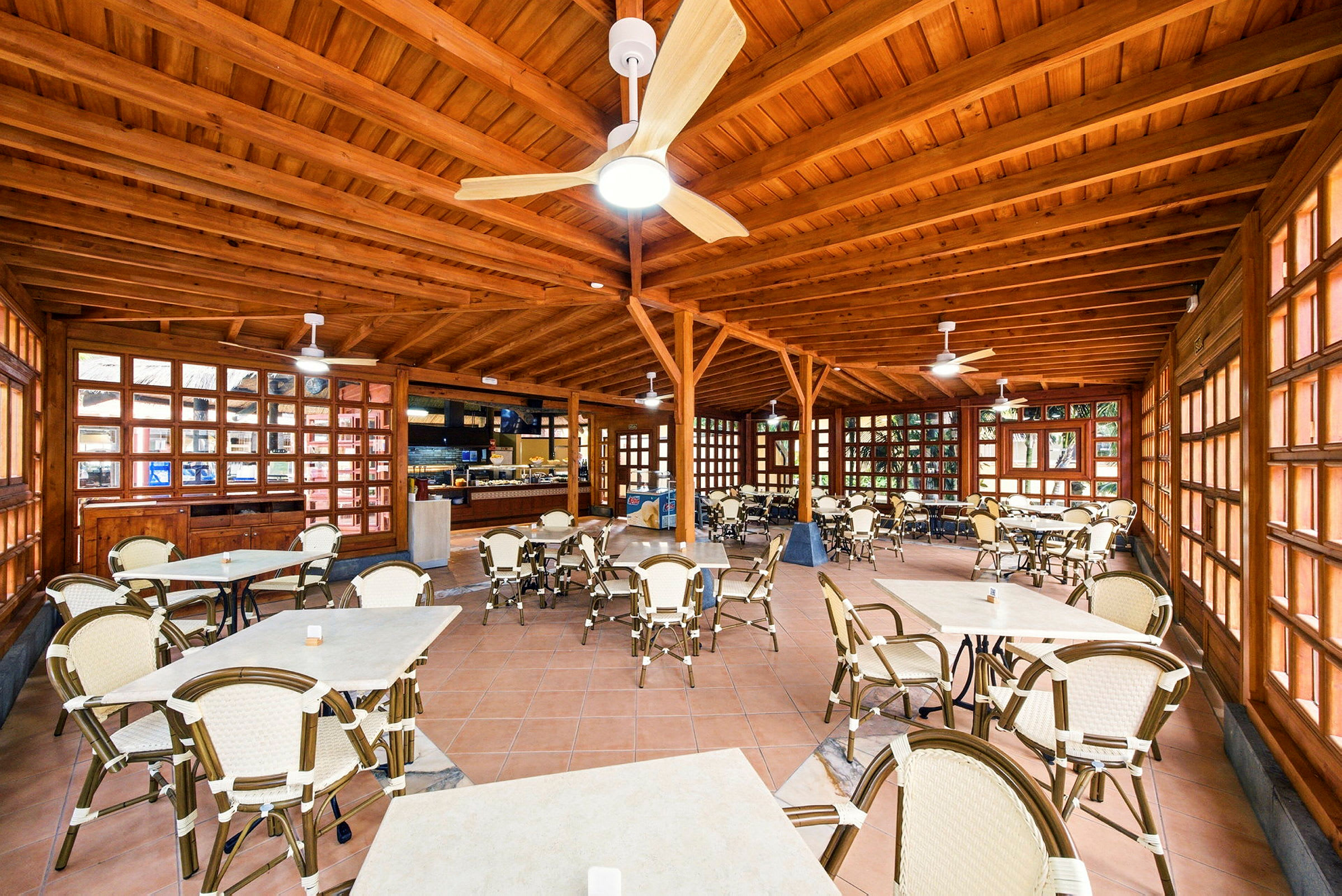 Tilava kahvila-alue, jossa on puukalusteet ja kattotuulettimet. (Tekoälyn luoma teksti)