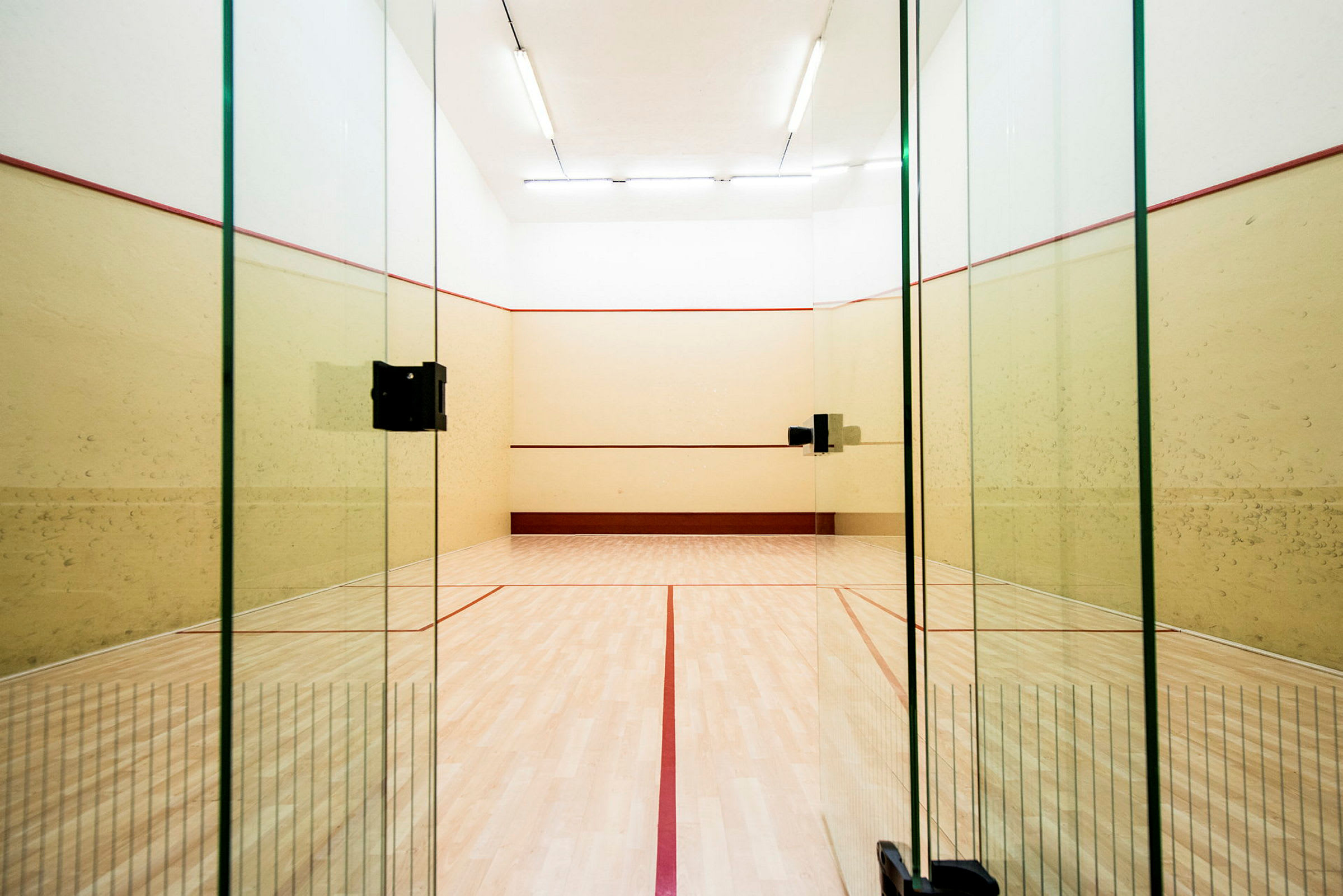 Squashkenttä, jossa on lasiovet ja vaaleat seinät. (Tekoälyn luoma teksti)