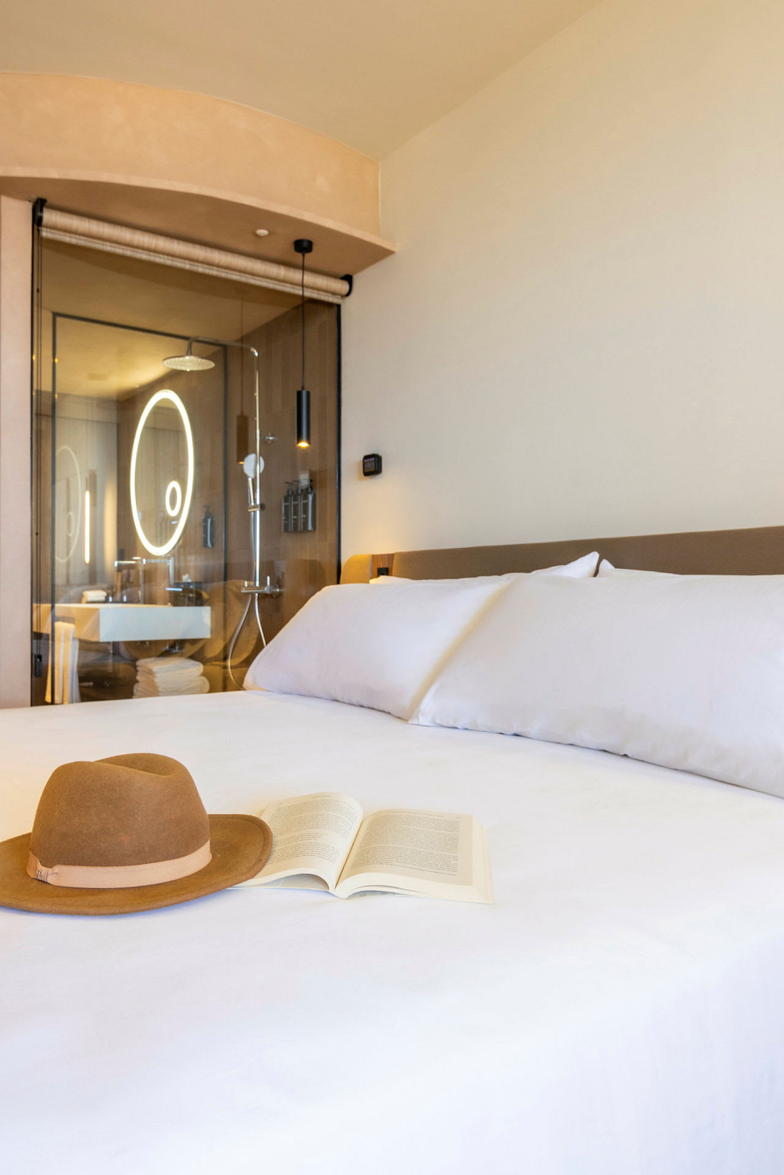 Hotellihuone, jossa sänky, hatu ja kirja aseteltuna siihen. Taustalla näkyy moderni kylpyhuone. (Tekoälyn luoma teksti)