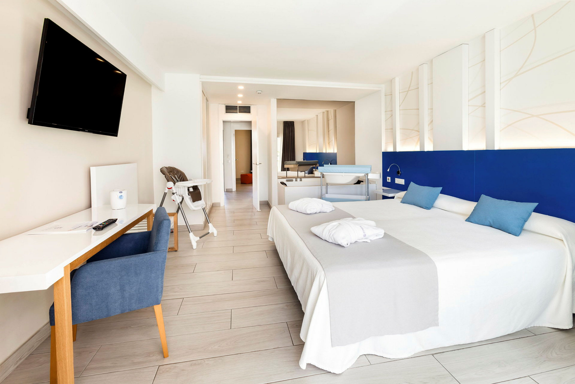 Hotellihuone, jossa on parisänky, kirjoituspöytä, televisio ja lasten tuoli. (Tekoälyn luoma teksti)
