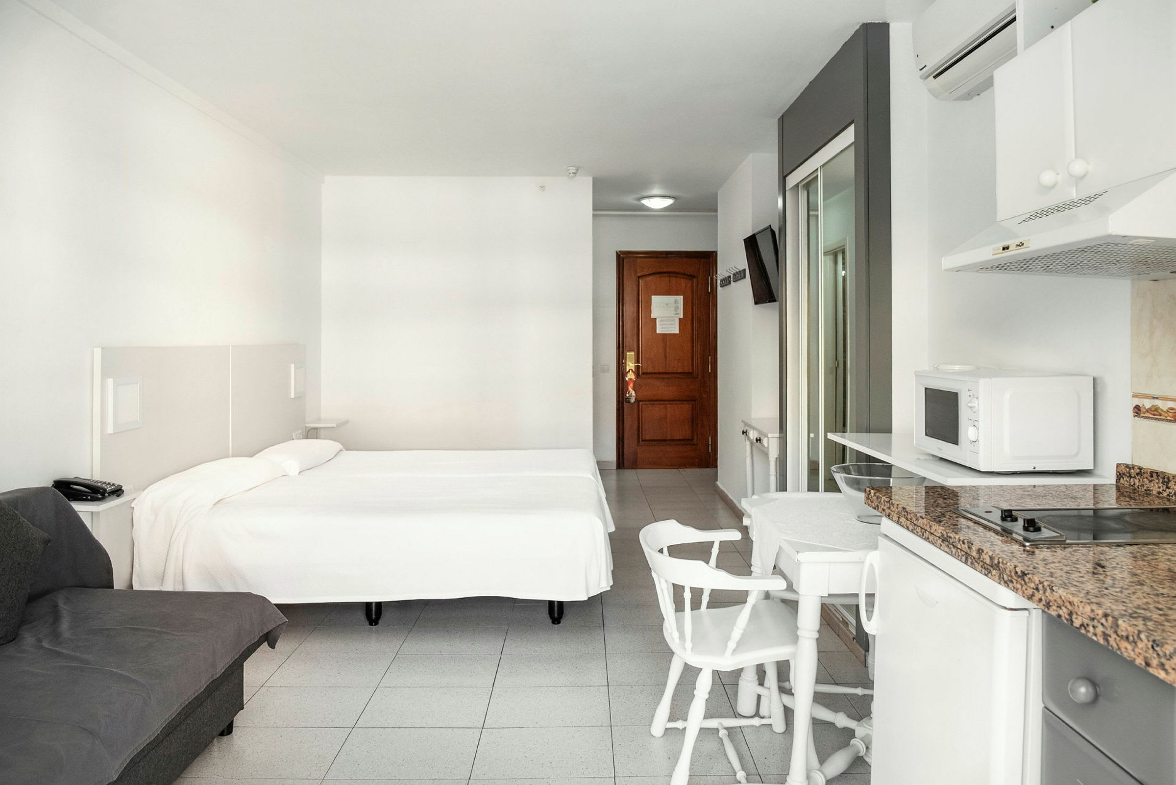 Hotellihuone, jossa parivuode, sohva, ruokapöytä tuoleineen ja minikeittiö. (Tekoälyn luoma teksti)